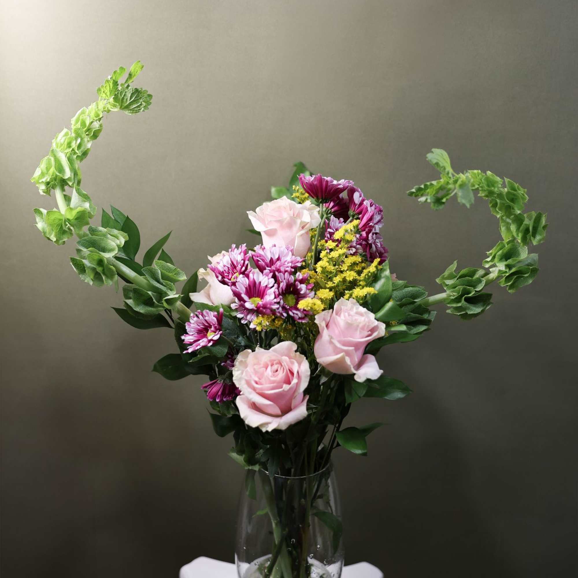 Pink roses and purple daisies in a clear glass vase