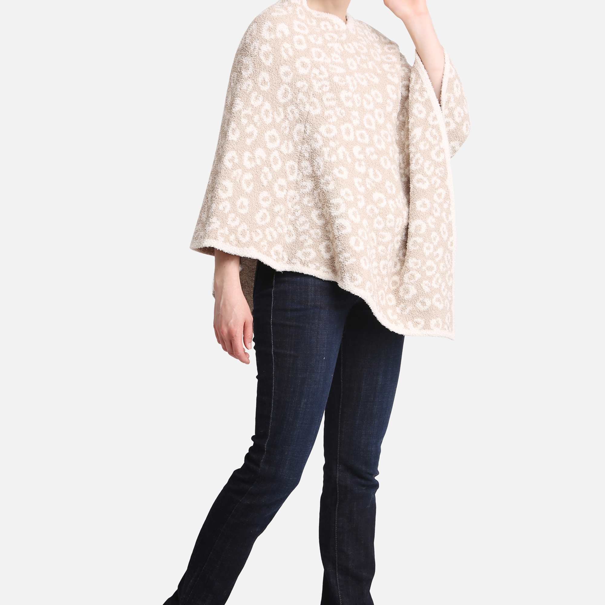 Woman wearing a beige patterned poncho with dark jeans and black heeled boots