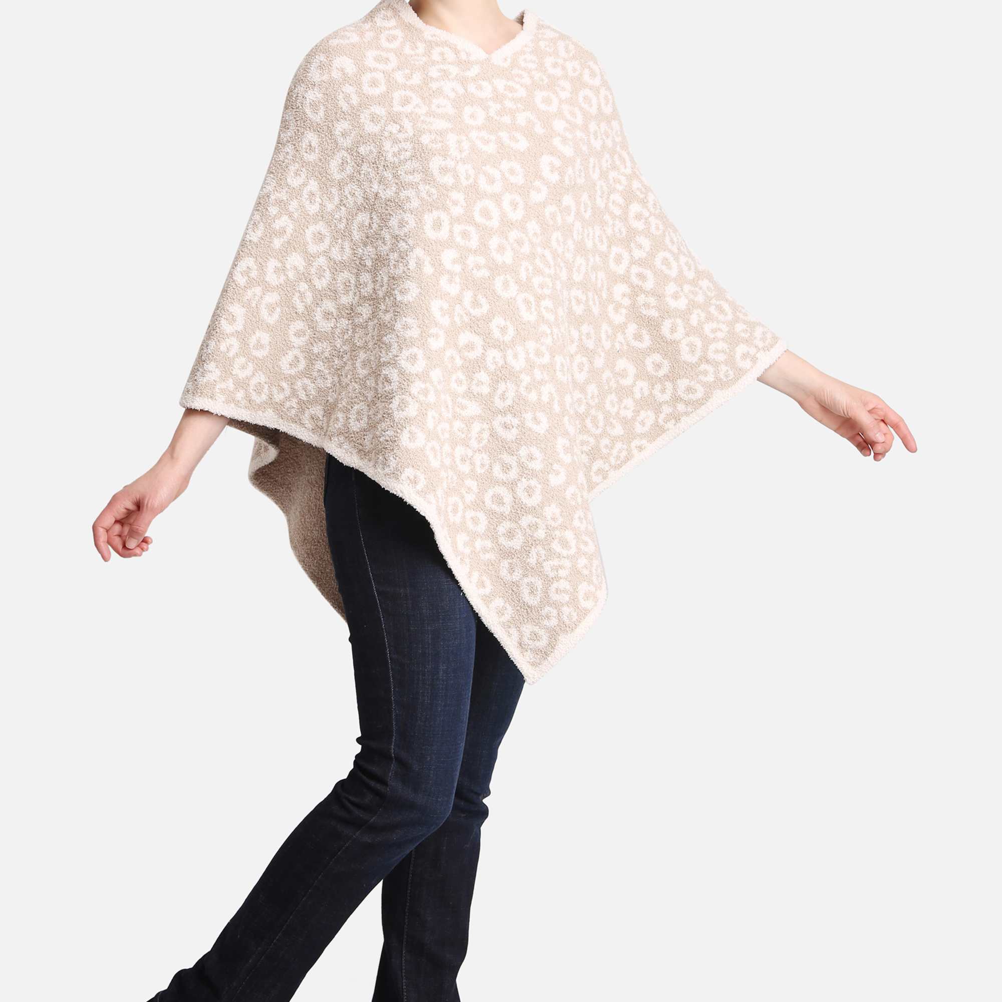 Person wearing a beige and white patterned knit poncho with dark jeans and black boots
