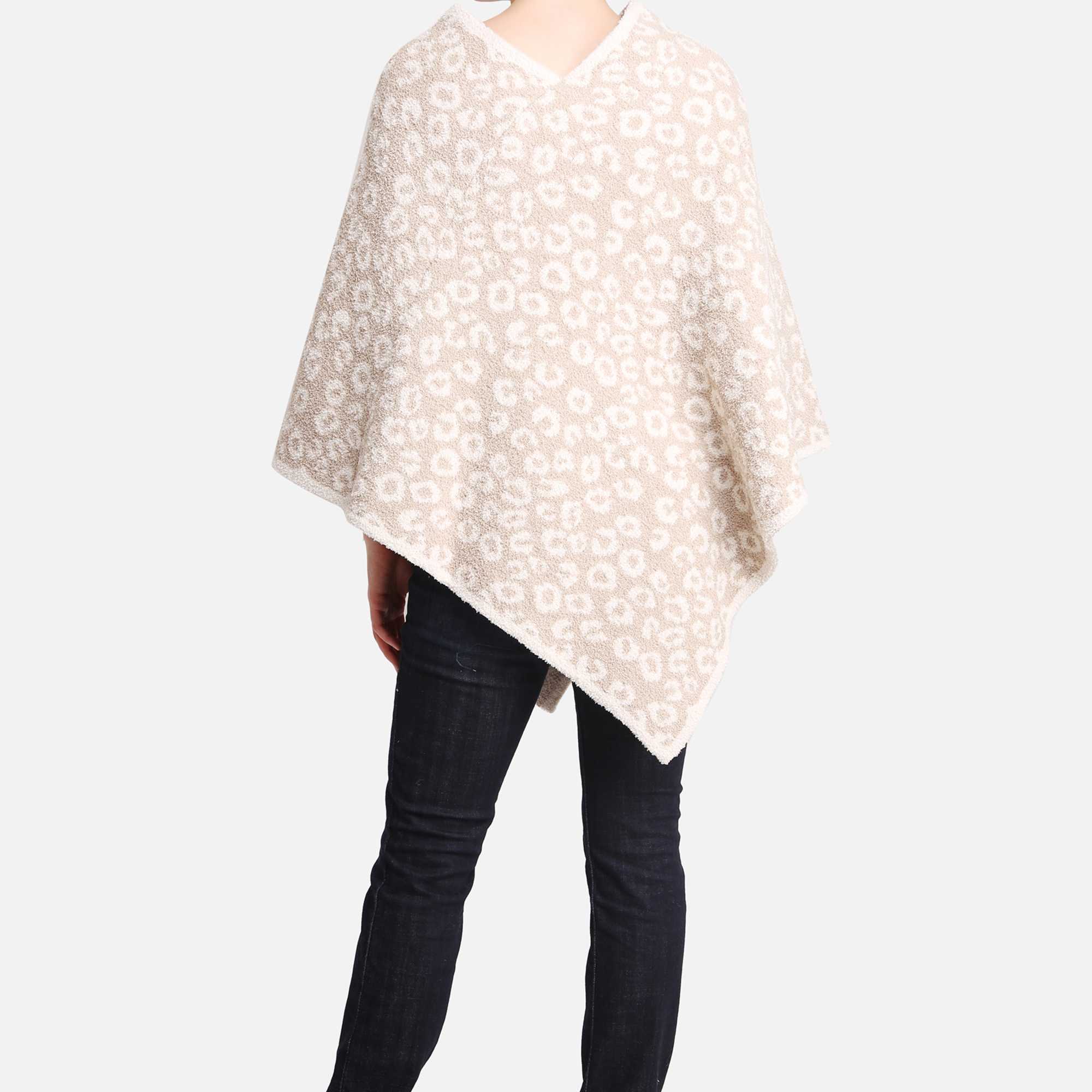 Person wearing a beige and white patterned poncho with dark jeans, viewed from the back.