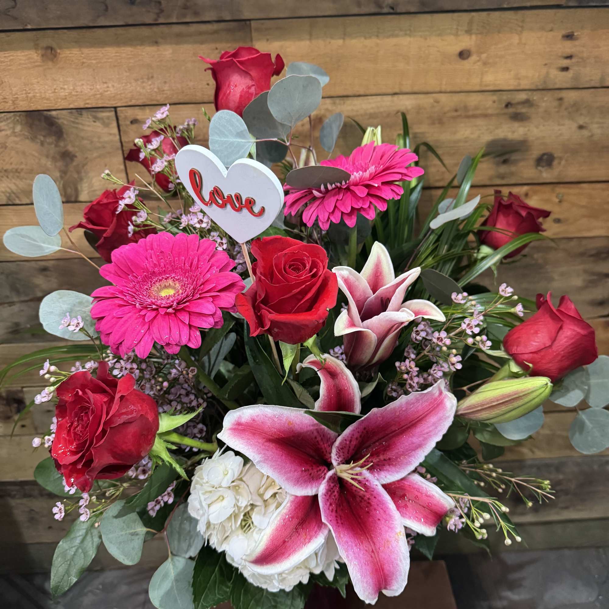 Bouquet of red roses, pink gerberas, and a pink lily with a heart pick