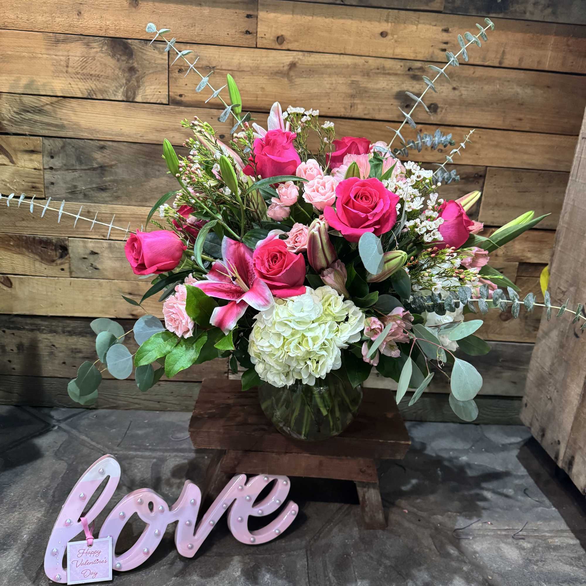 Pink rose and lily bouquet in a glass vase with a pink "love" sign
