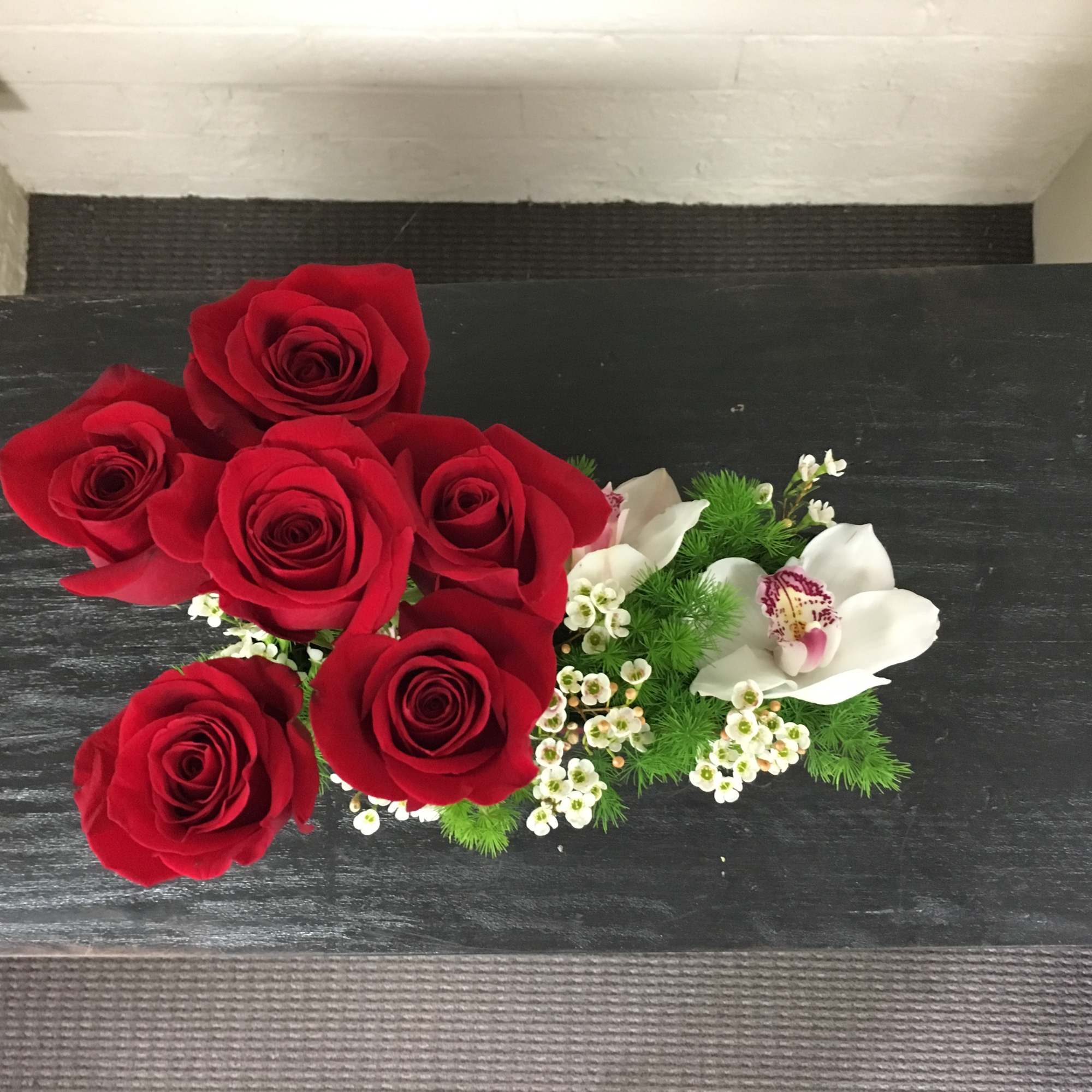 Red roses with white orchids and small white filler flowers on a black surface