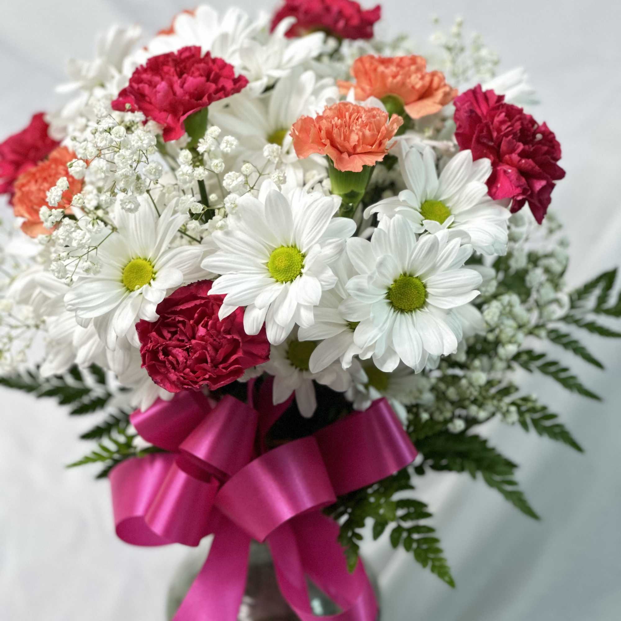 Bouquet of white daisies and pink carnations with a magenta ribbon in a vase