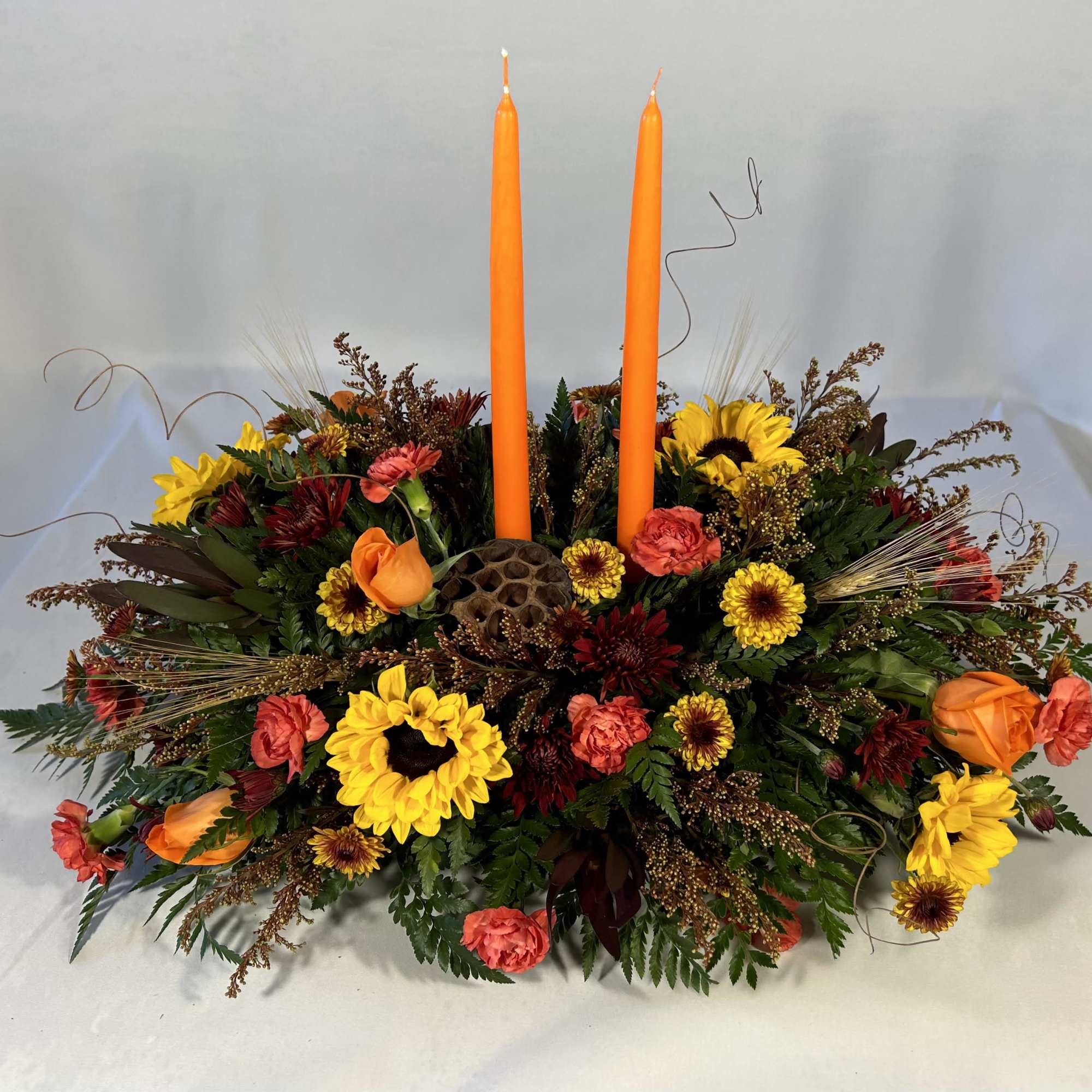 Low floral centerpiece with two orange taper candles and mixed autumn blooms