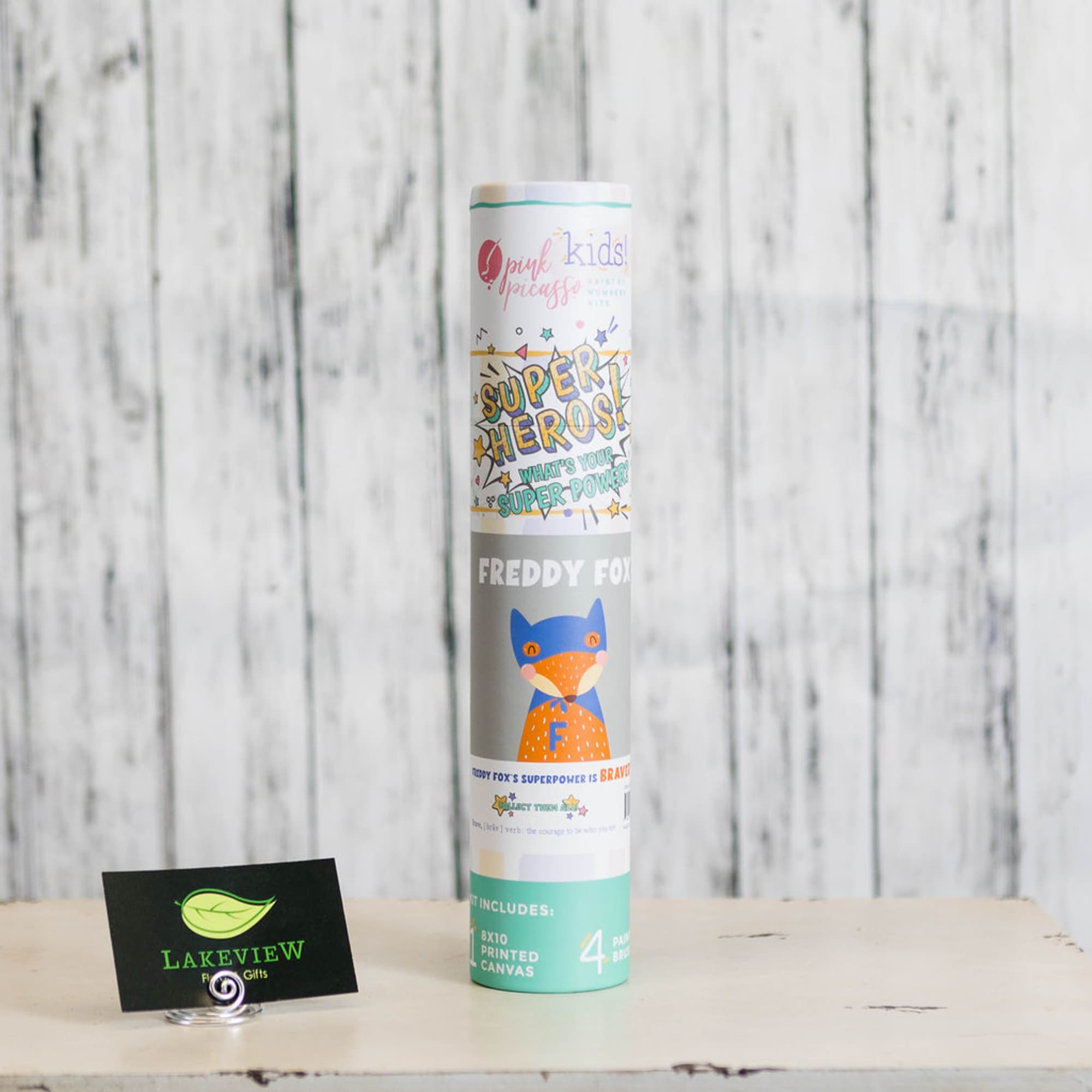 A tall cylindrical tube with colorful children's artwork stands on a table.
