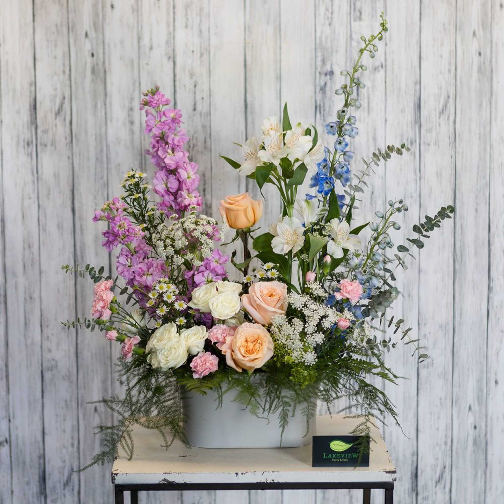 Mixed bouquet in a white container with pink, peach, white, and blue flowers