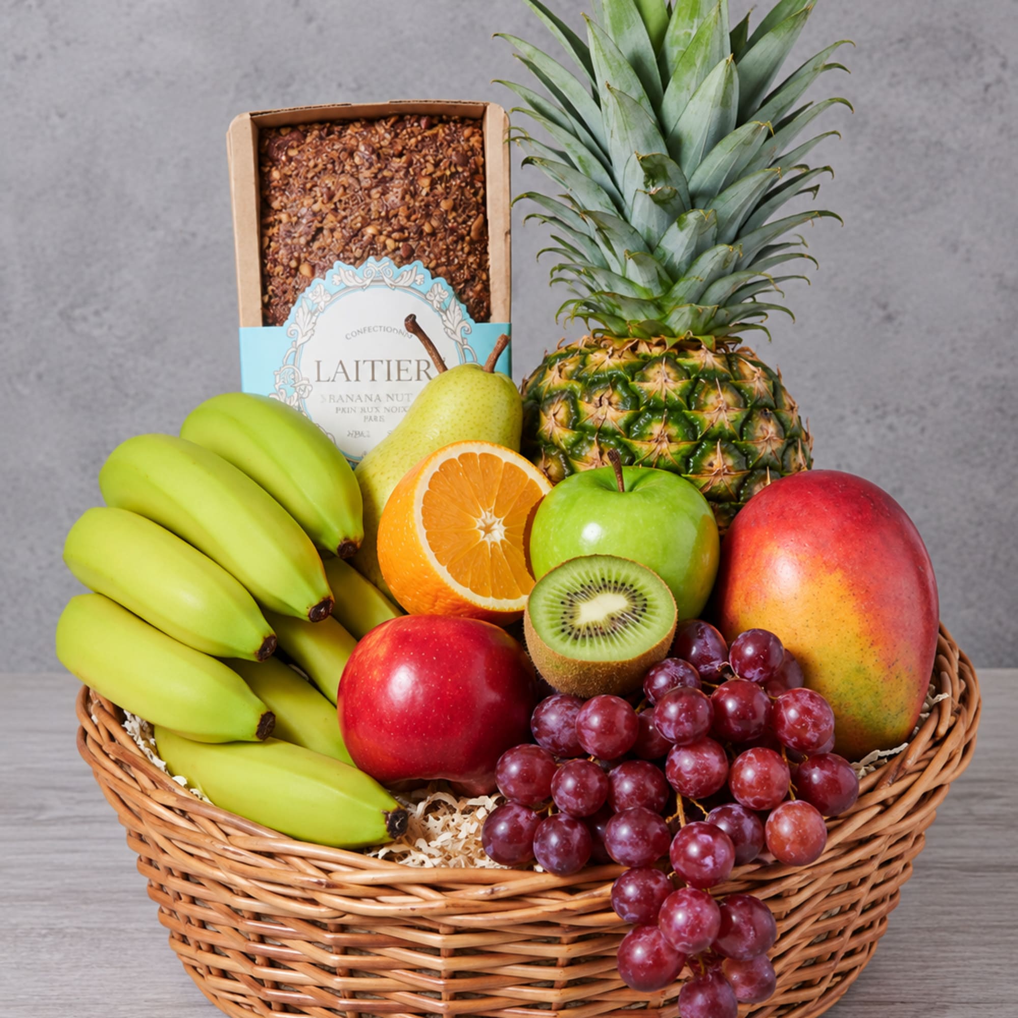 Fruit basket with bananas, pineapple, grapes, mango, apple, pear, kiwi, orange, and a nut bar box