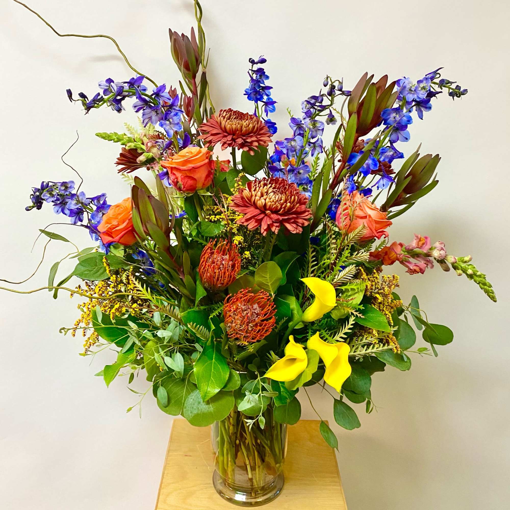 Tall mixed bouquet in a clear glass vase with orange, blue, yellow, and burgundy flowers