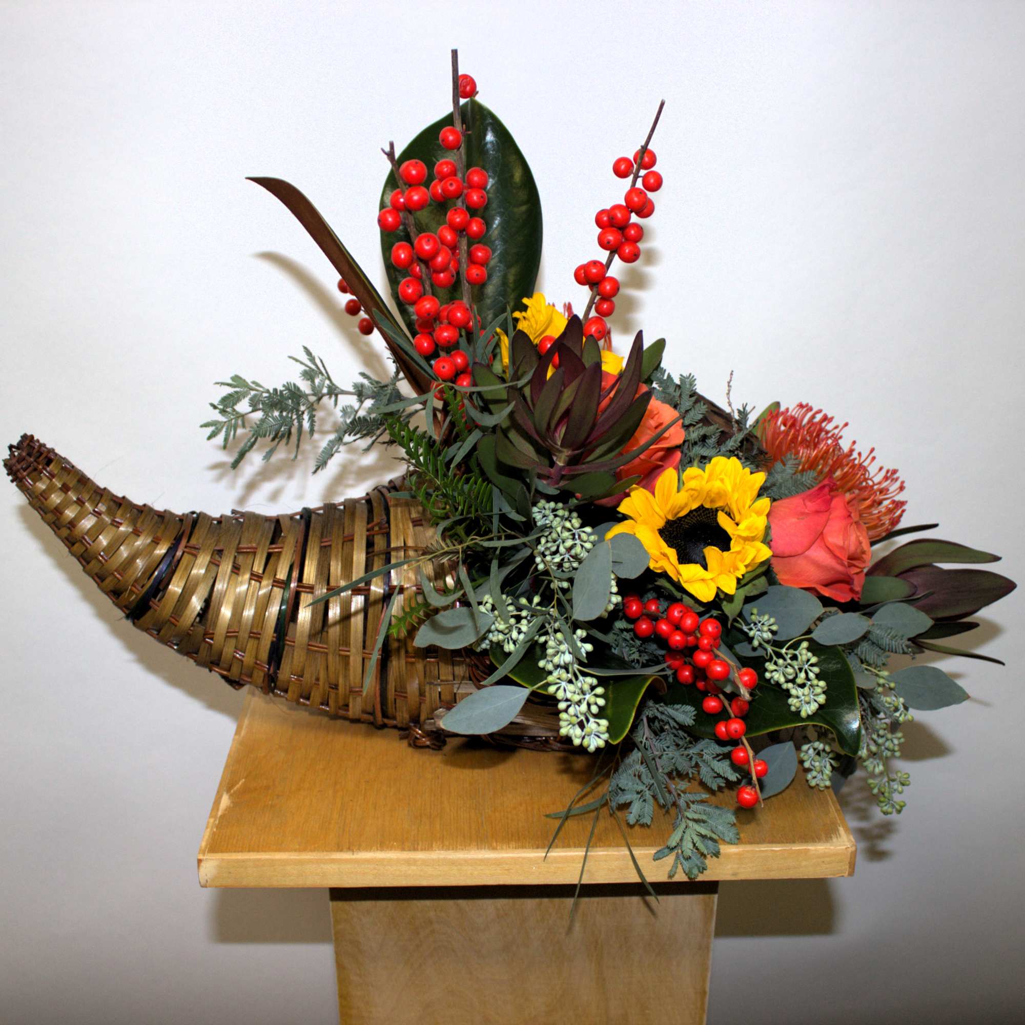 Horn-shaped floral arrangement with red berries, sunflowers, and roses