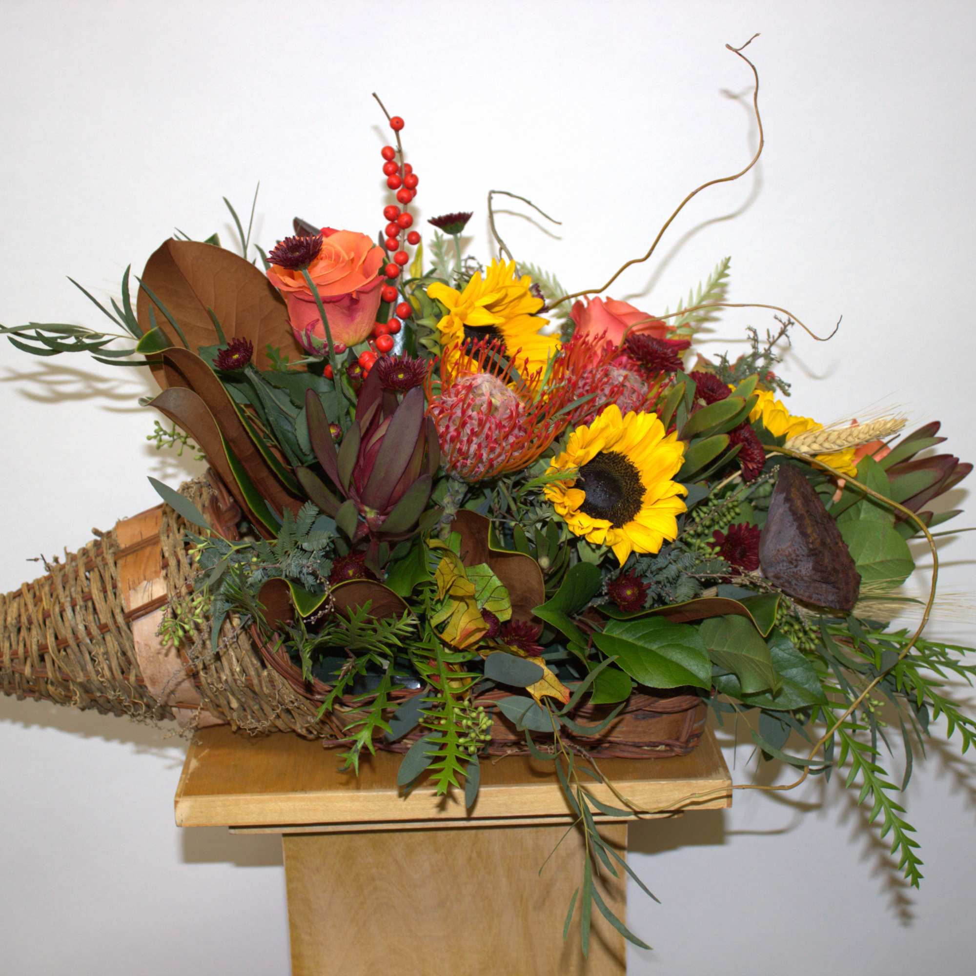 Mixed bouquet with sunflowers, roses, and protea in a woven cone holder