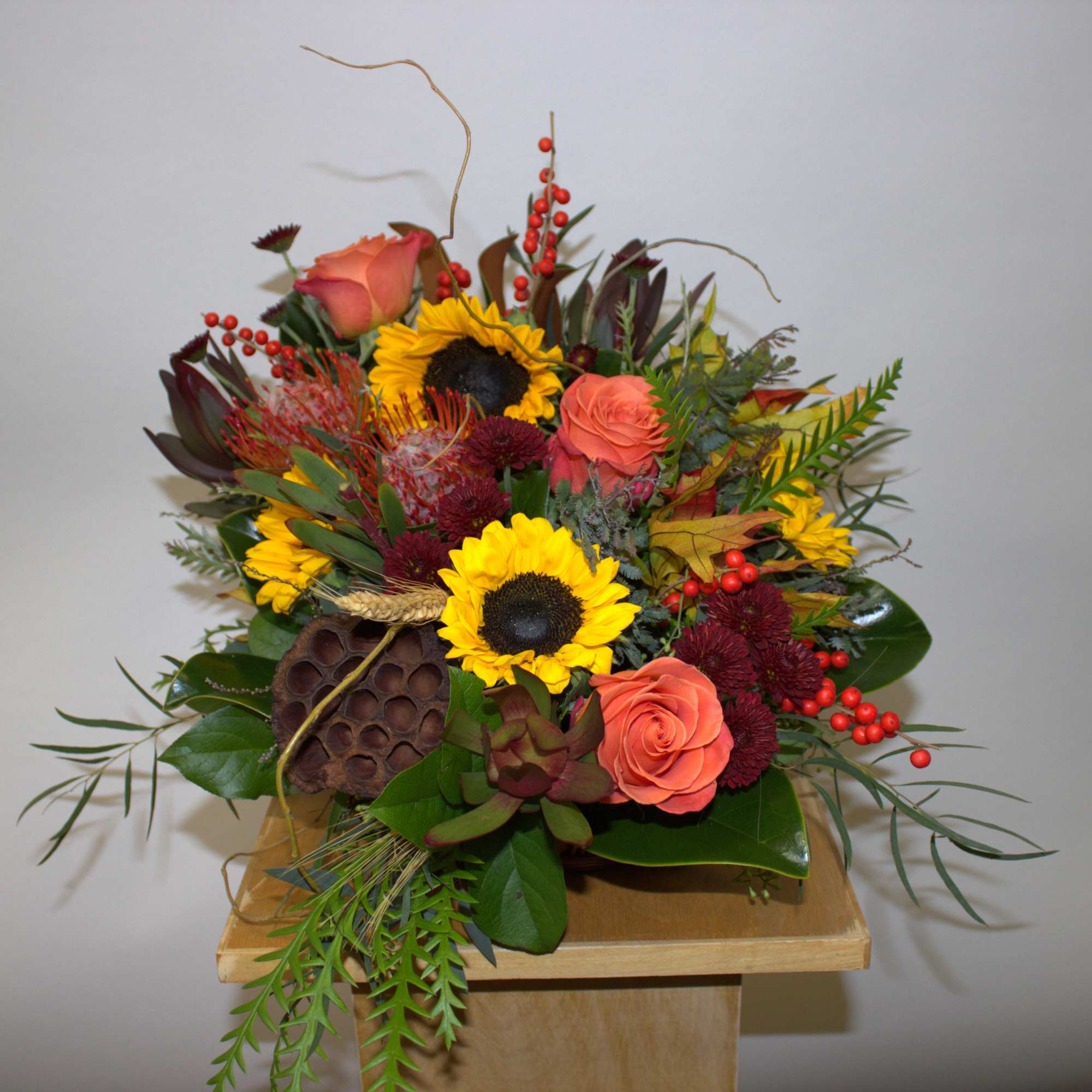 Mixed bouquet with sunflowers, coral roses, and red berries in a wooden container