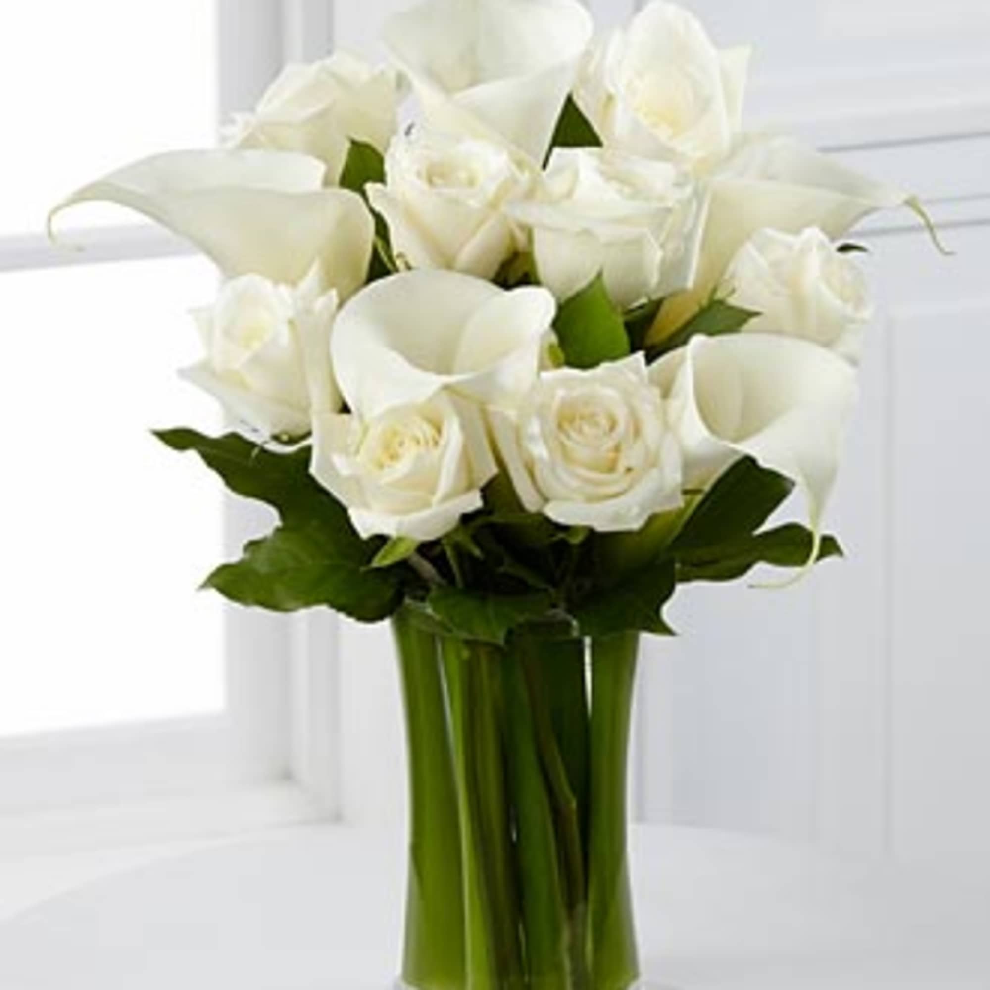 White roses and calla lilies in a clear glass vase