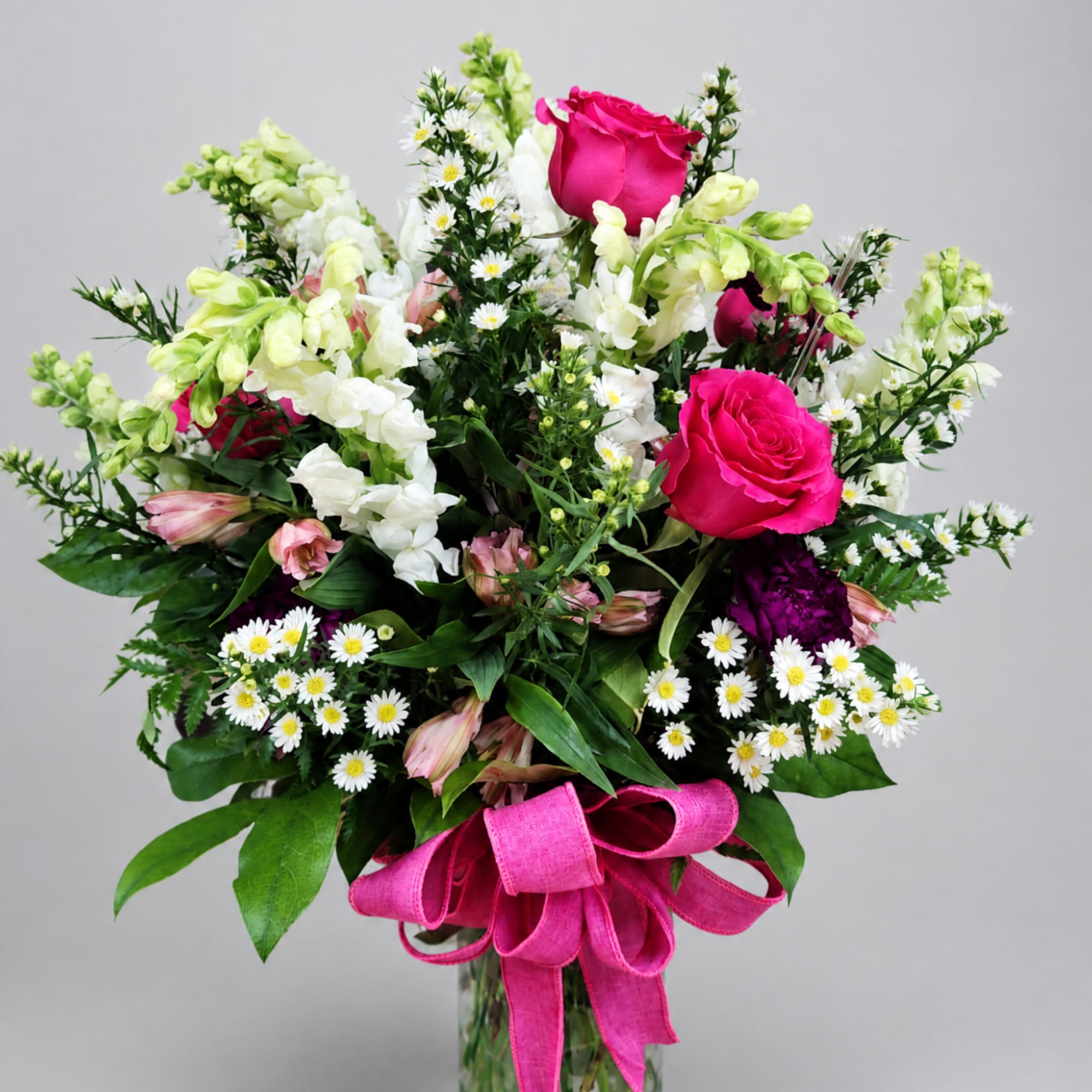 Bouquet of hot pink roses, white snapdragons, and small daisies with a pink ribbon