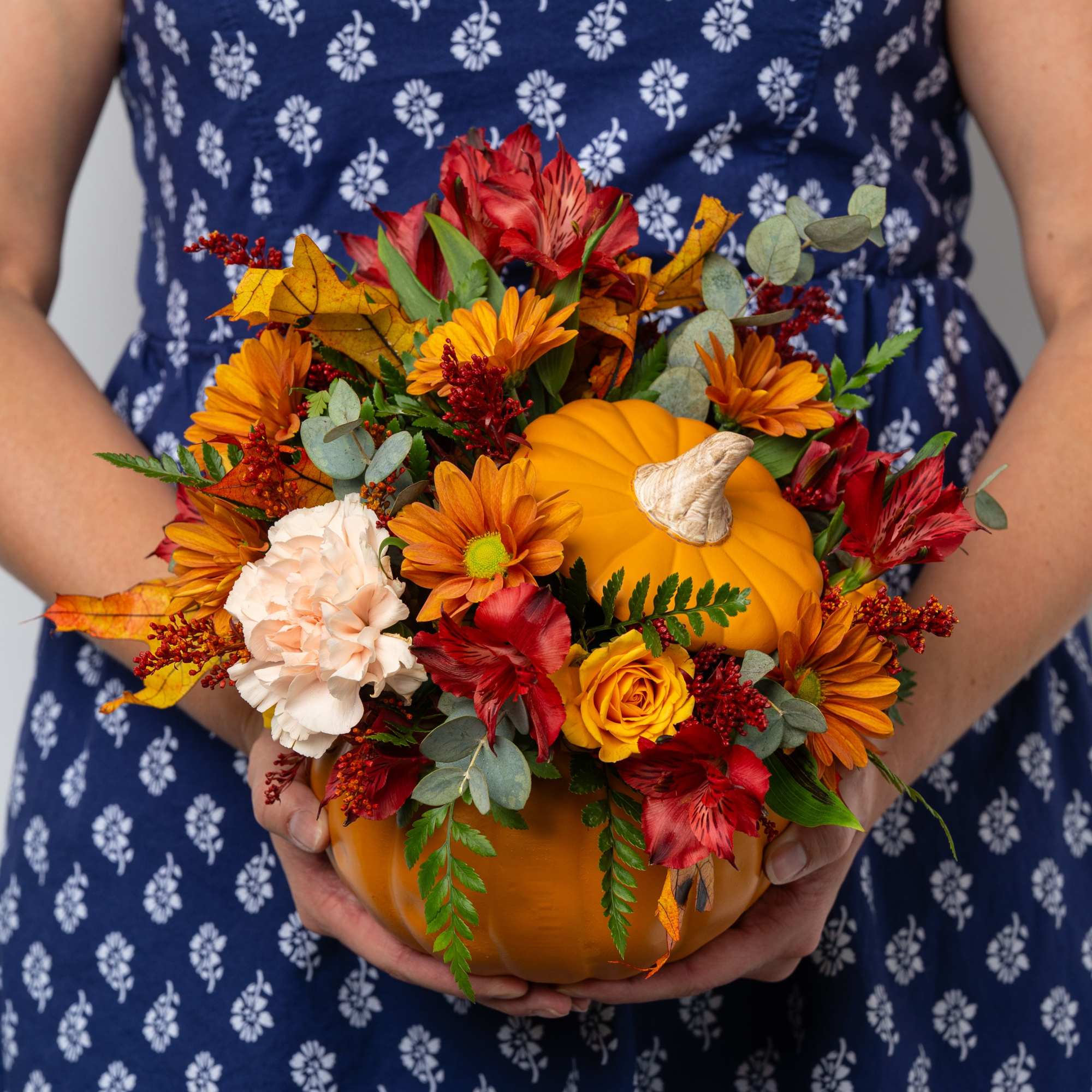 Autumn floral arrangement in a pumpkin container with orange and red blooms