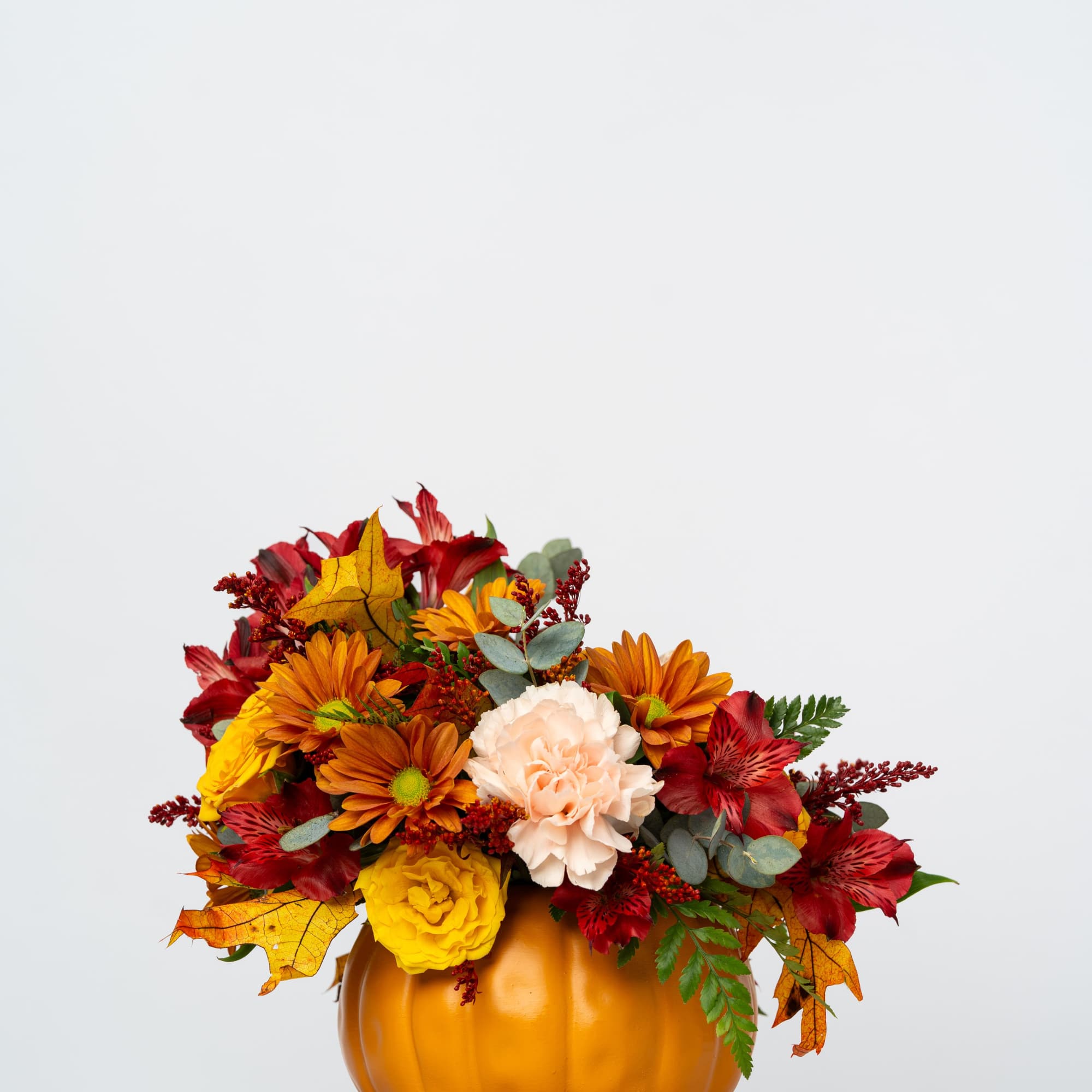 Fall floral arrangement in a pumpkin-shaped container with red, orange, and yellow blooms