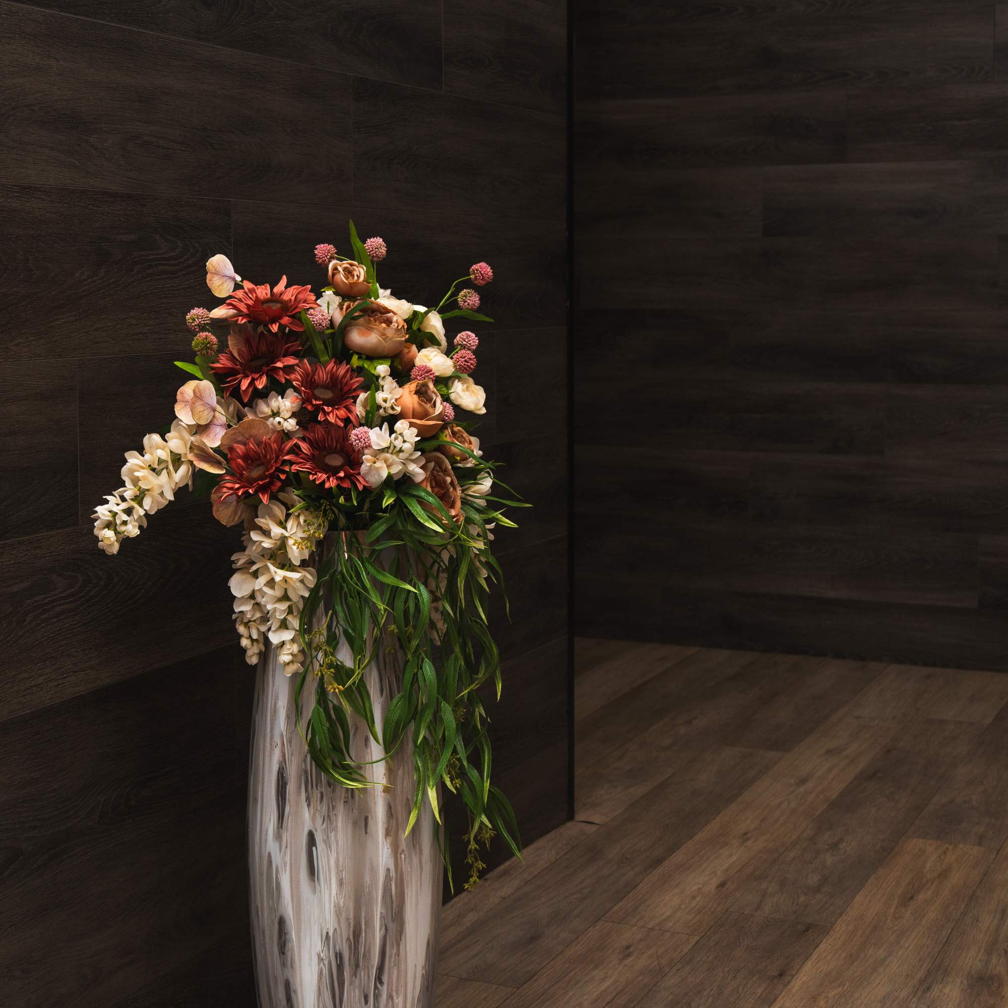 Tall floral arrangement in a white floor vase with red, cream, and pink blooms