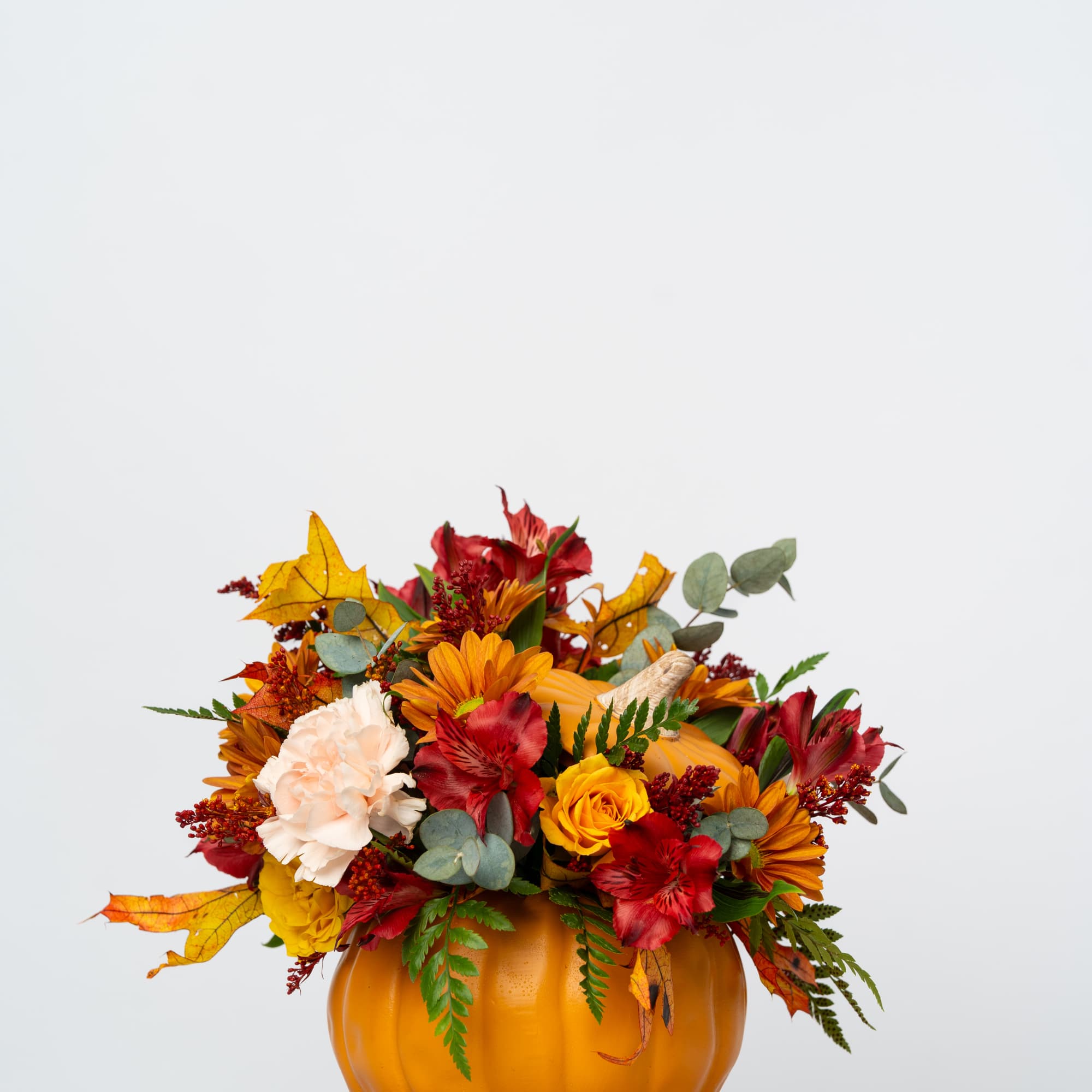 Autumn flower arrangement in a pumpkin-shaped container with red, orange, and cream blooms