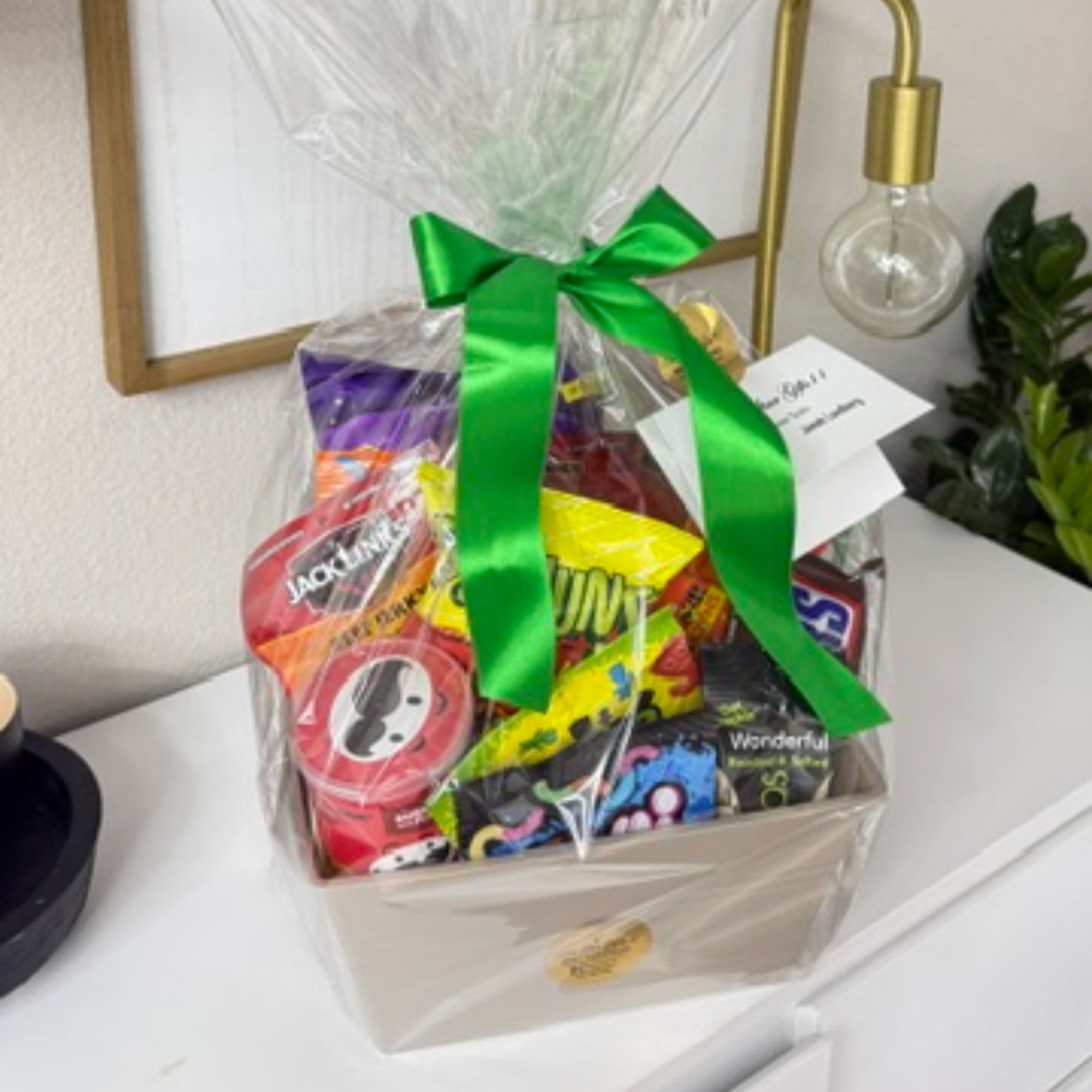 Gift basket of assorted candy wrapped in clear cellophane with a green ribbon