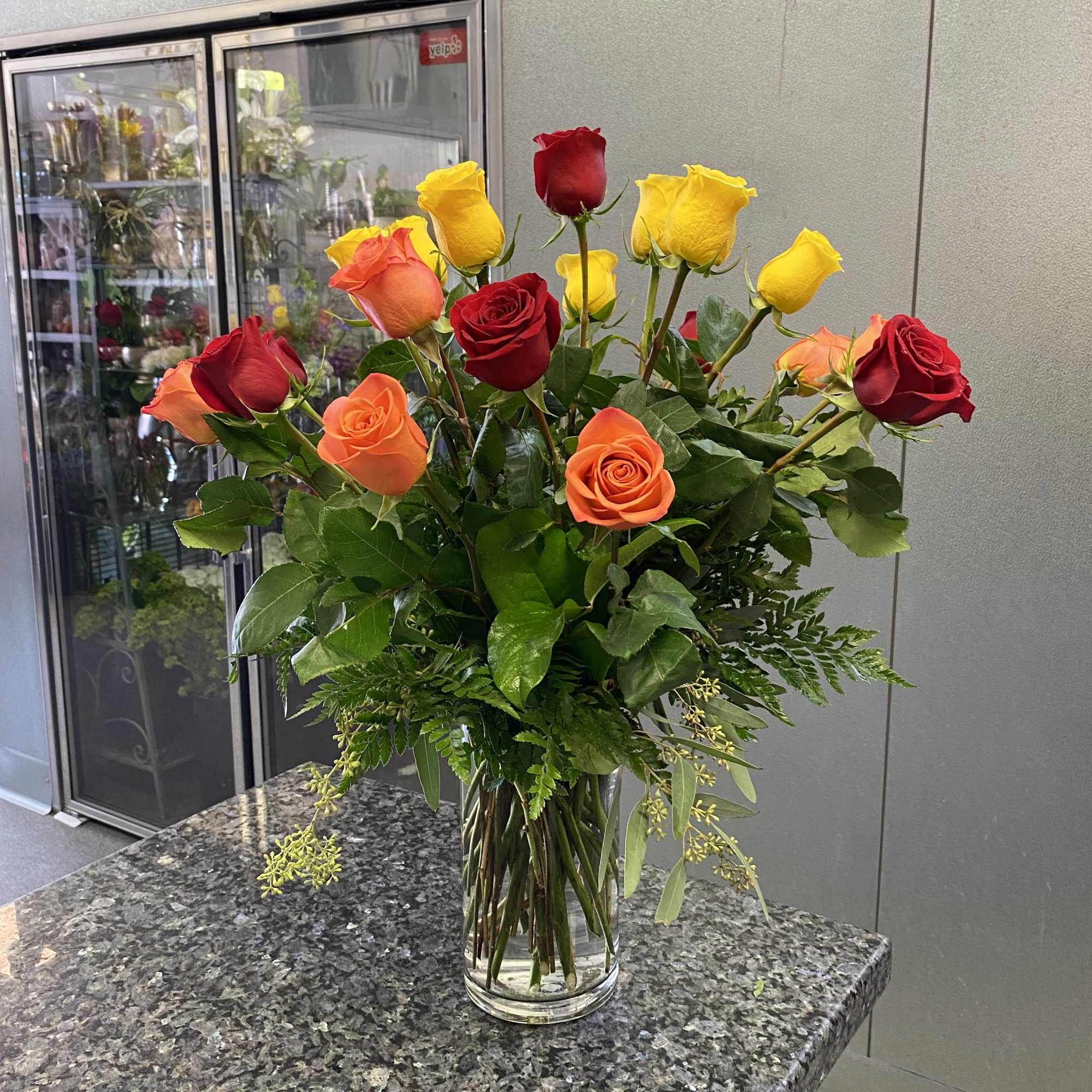 Bouquet of red, yellow, and orange roses in a clear glass vase