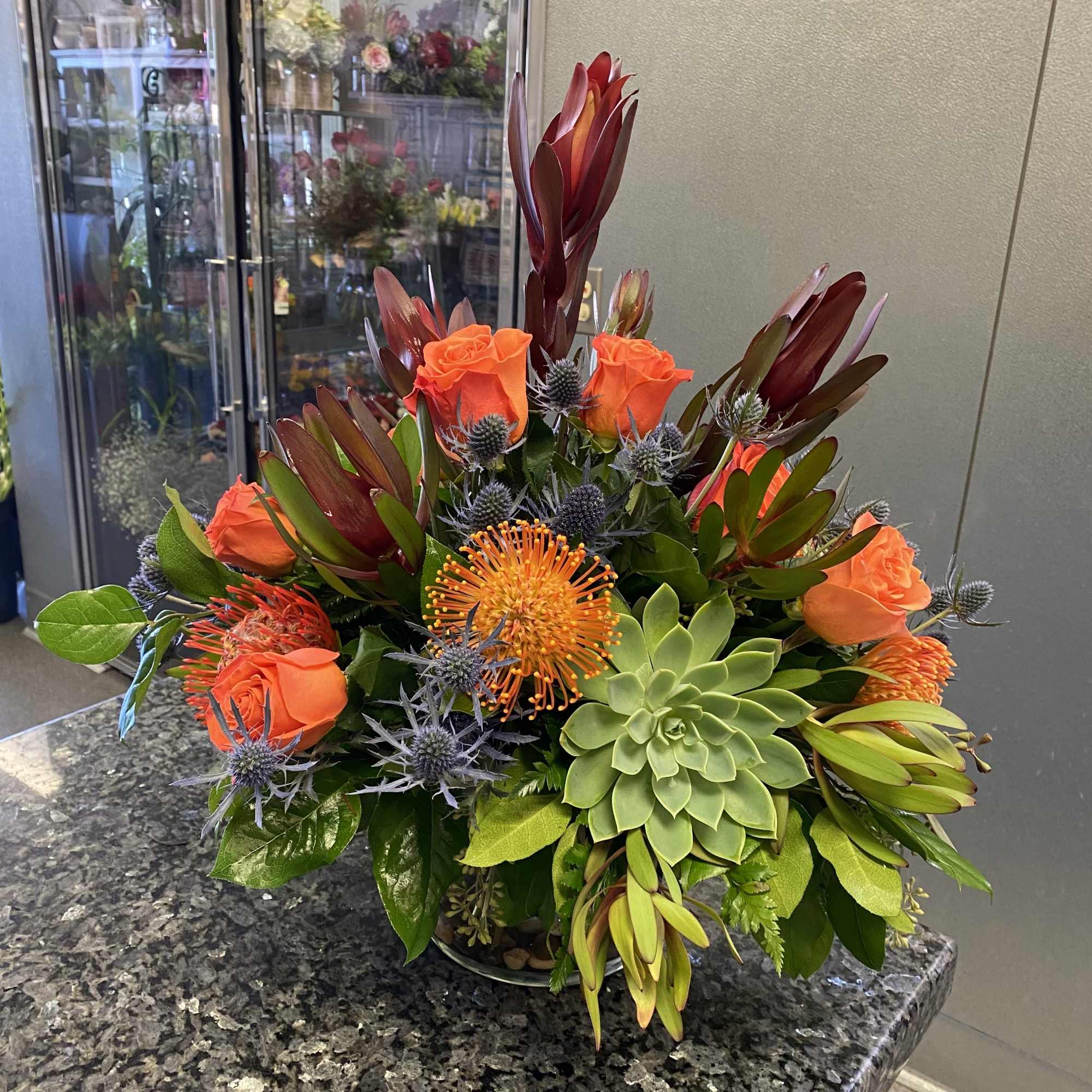 Orange roses and succulents in a low glass bowl