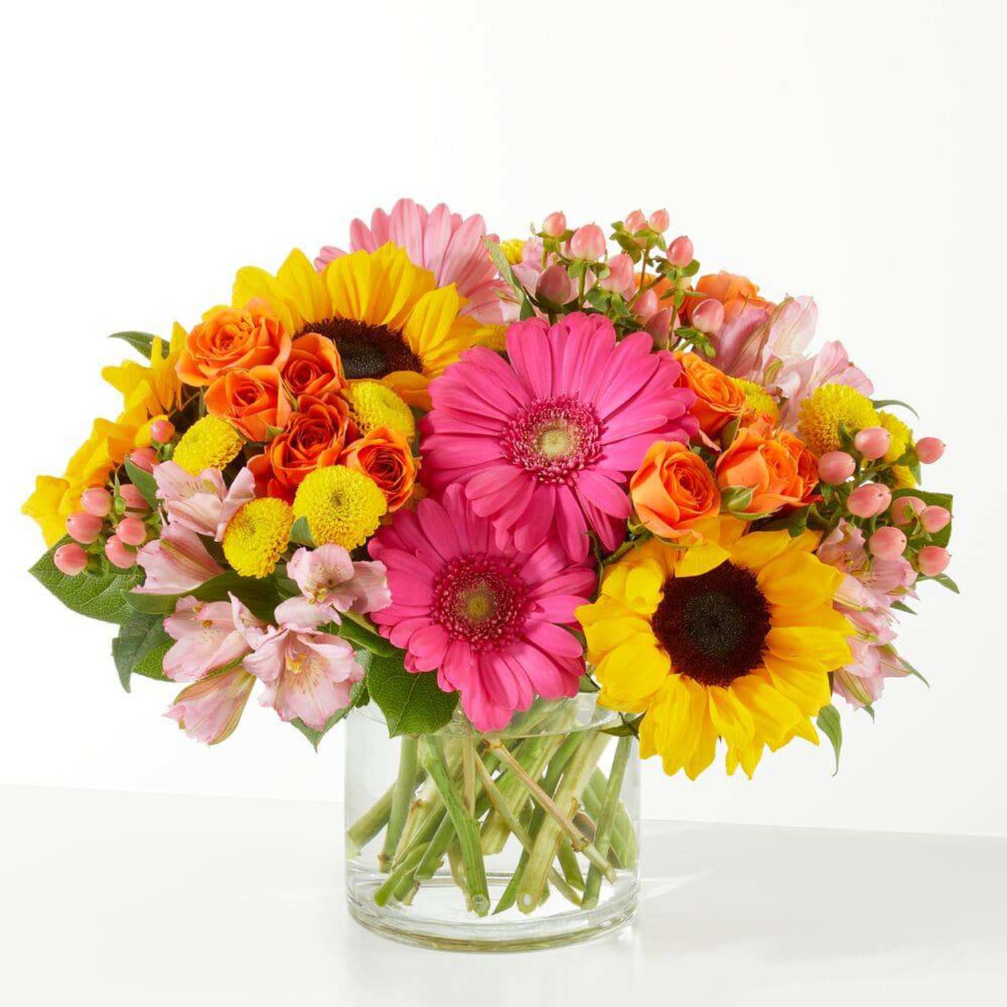 Bright mixed bouquet in a clear glass vase with sunflowers, gerbera daisies, and roses