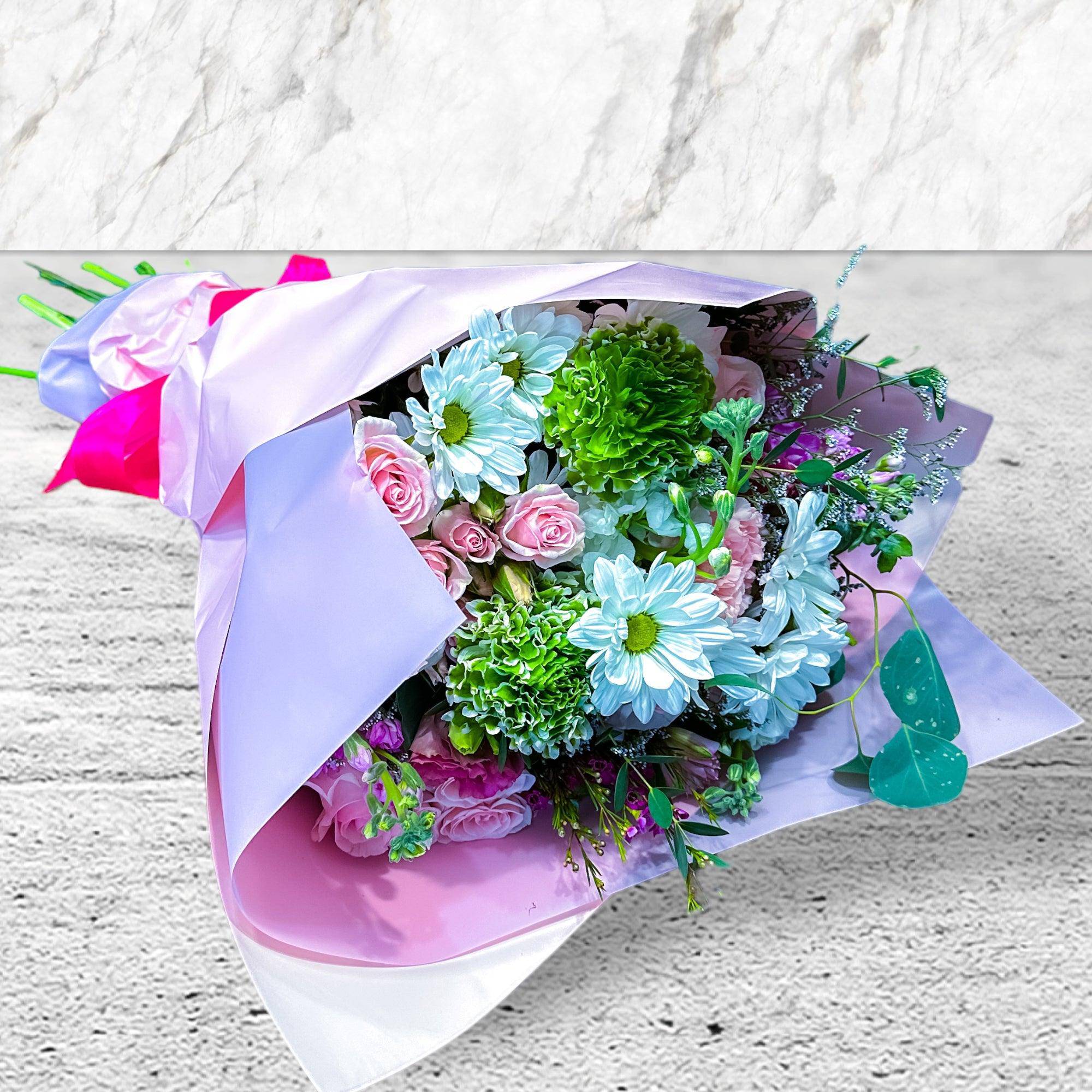 Bouquet of pink roses, blue daisies, and green carnations in pastel wrap