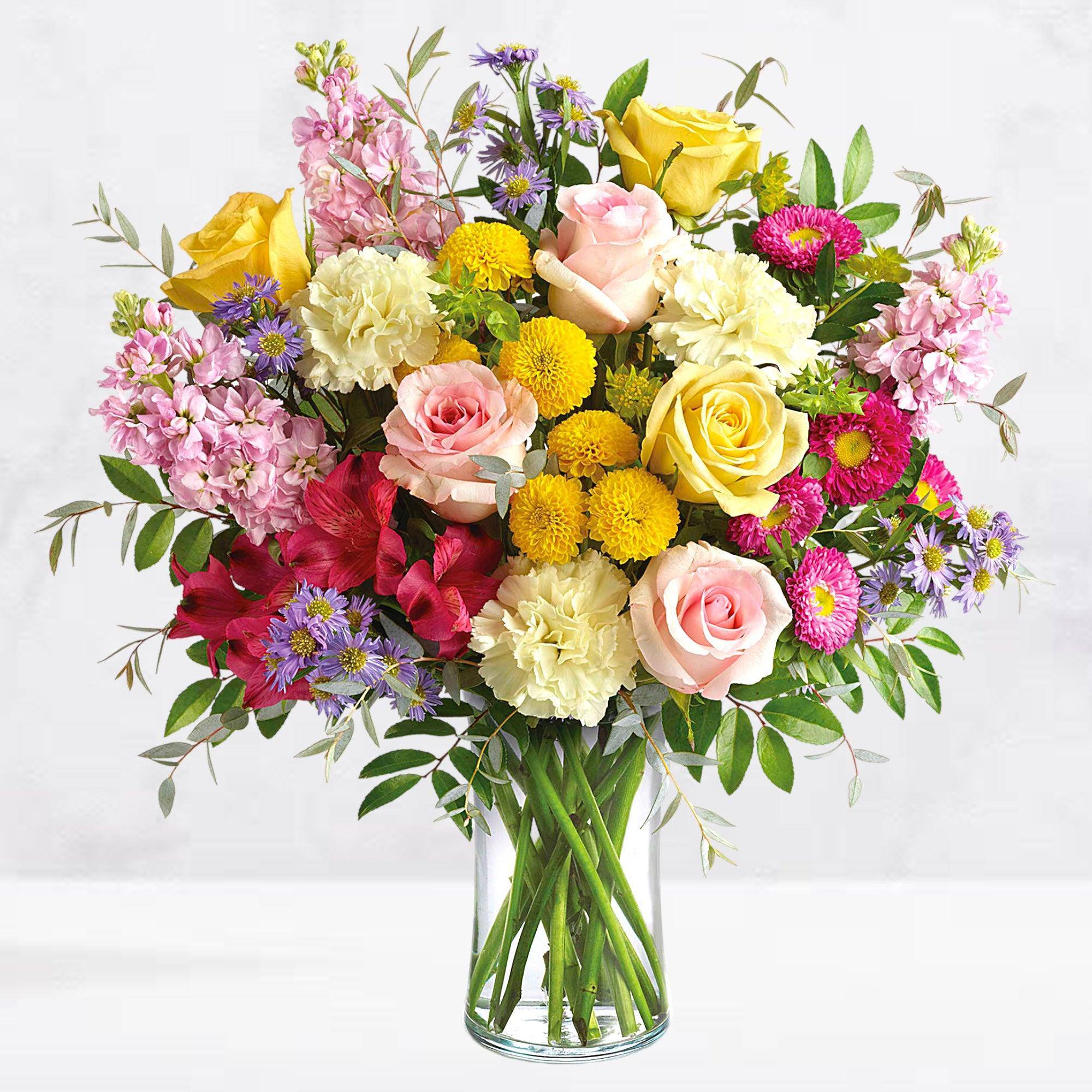 Mixed bouquet of roses, carnations, and daisies in a clear glass vase