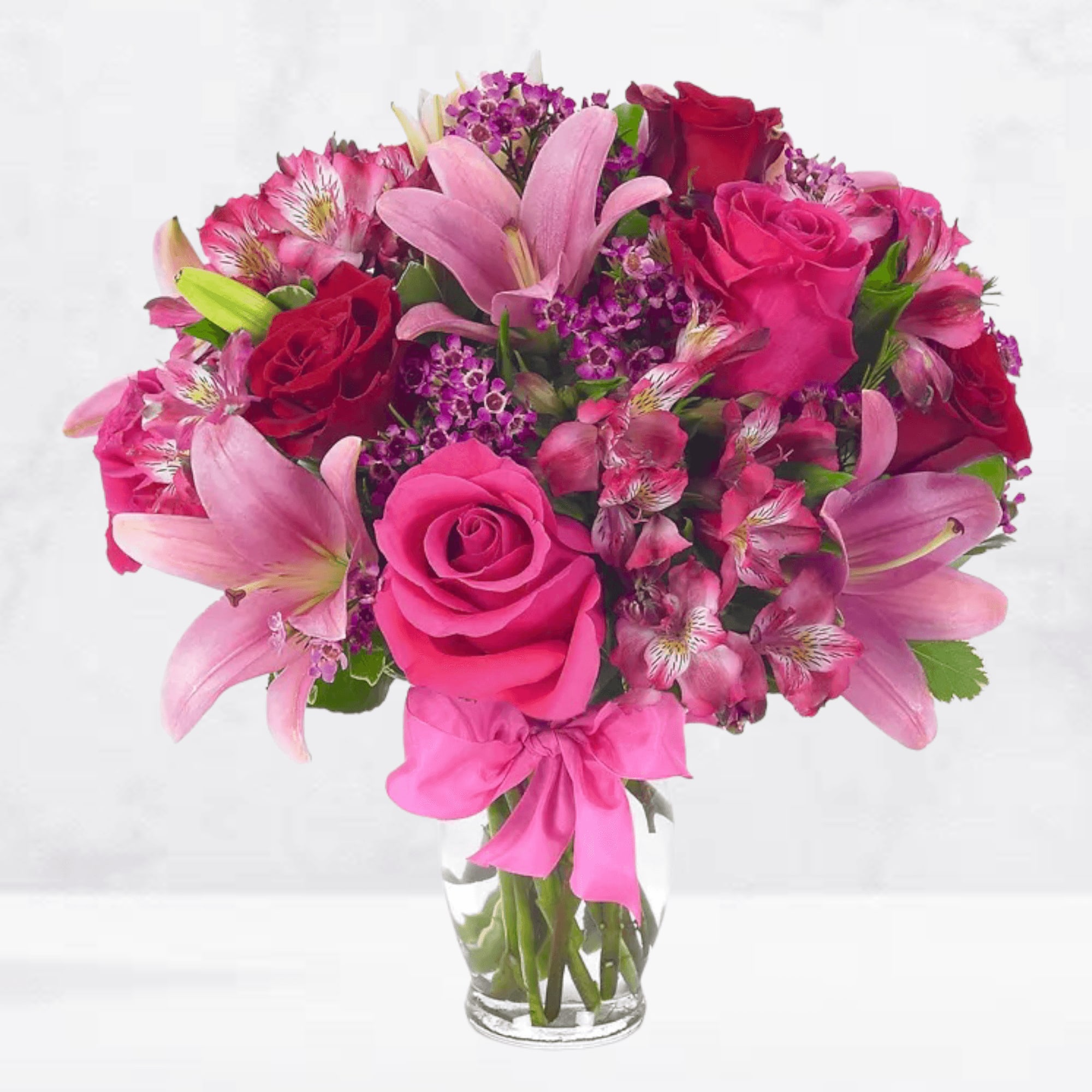 Pink and red bouquet of roses and lilies in a clear glass vase