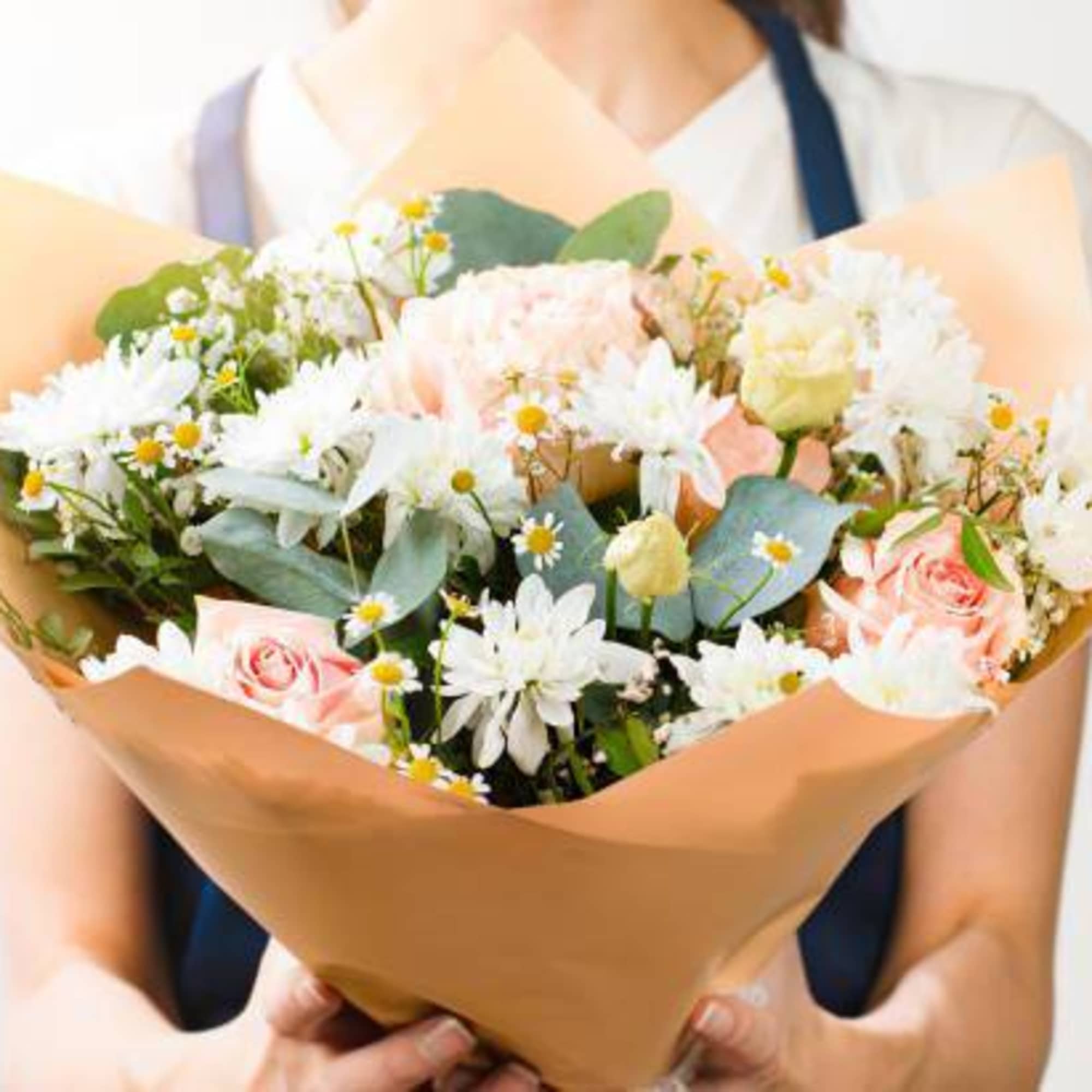 Person holding a bouquet of white and pale pink flowers wrapped in tan paper
