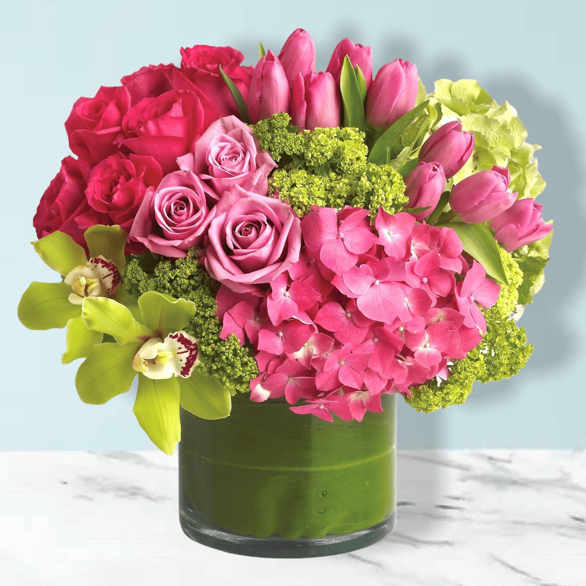 Pink roses, tulips, hydrangea, and green orchids in a glass vase