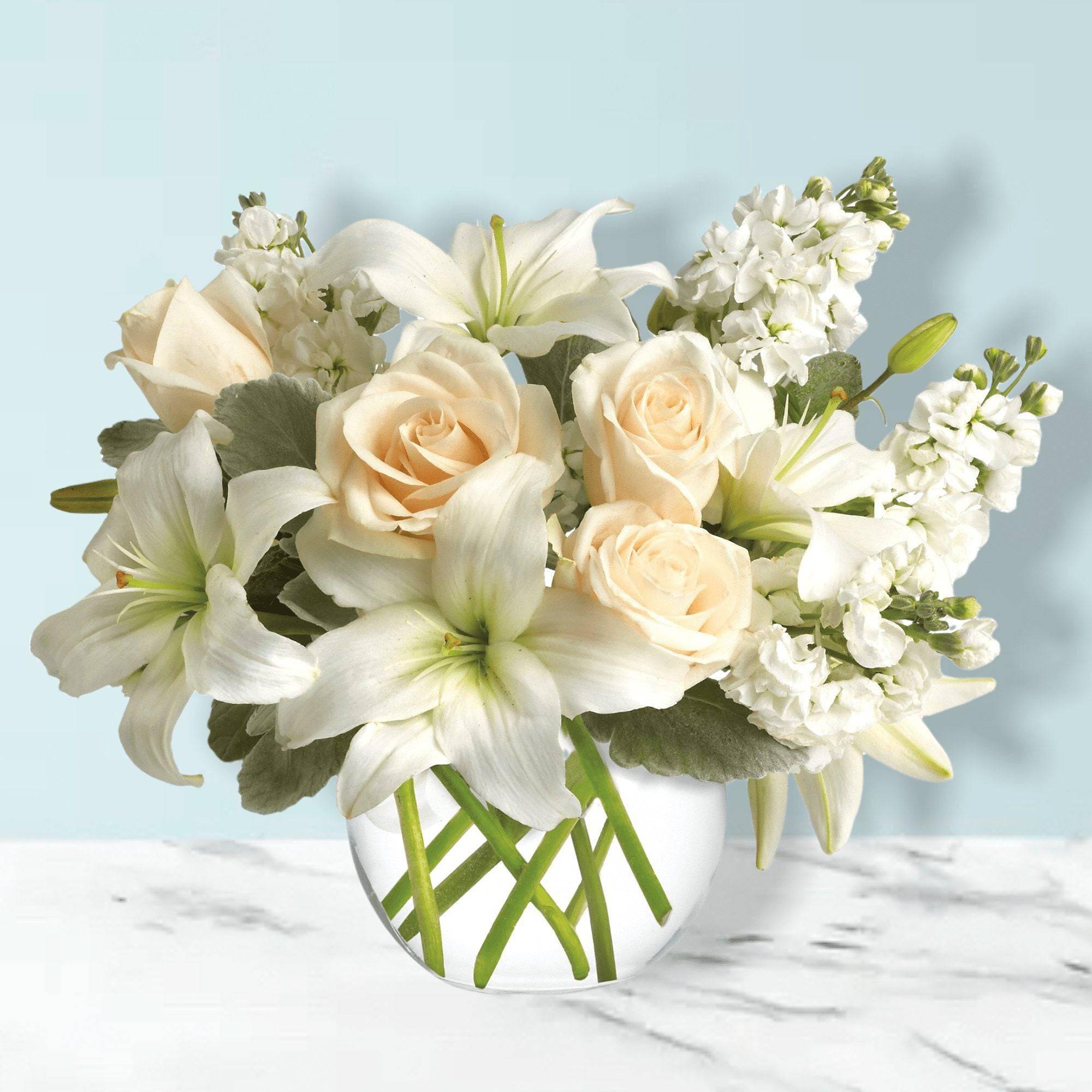 White lilies and cream roses arranged in a clear glass vase