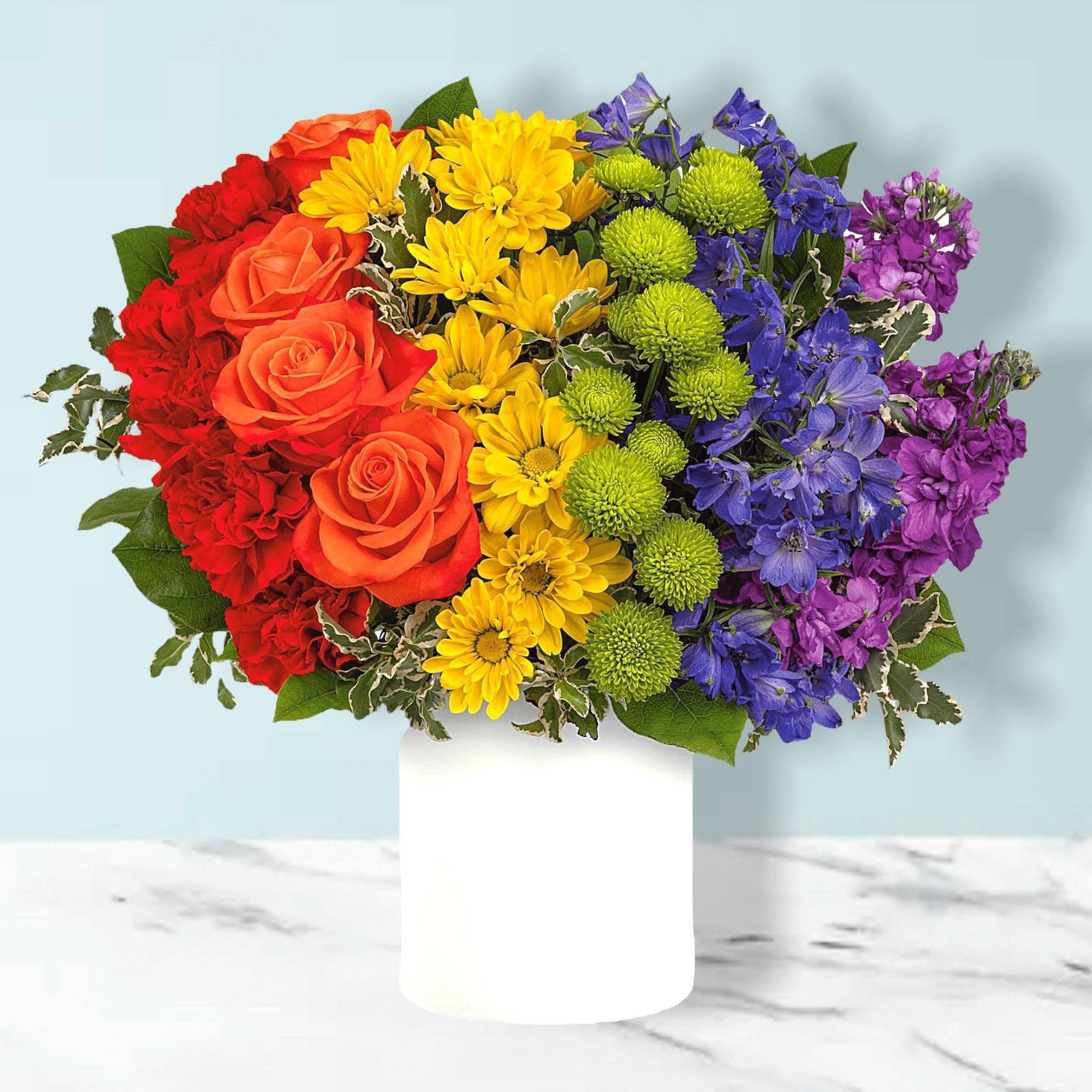 Rainbow bouquet of roses, daisies, and purple blooms in a white vase