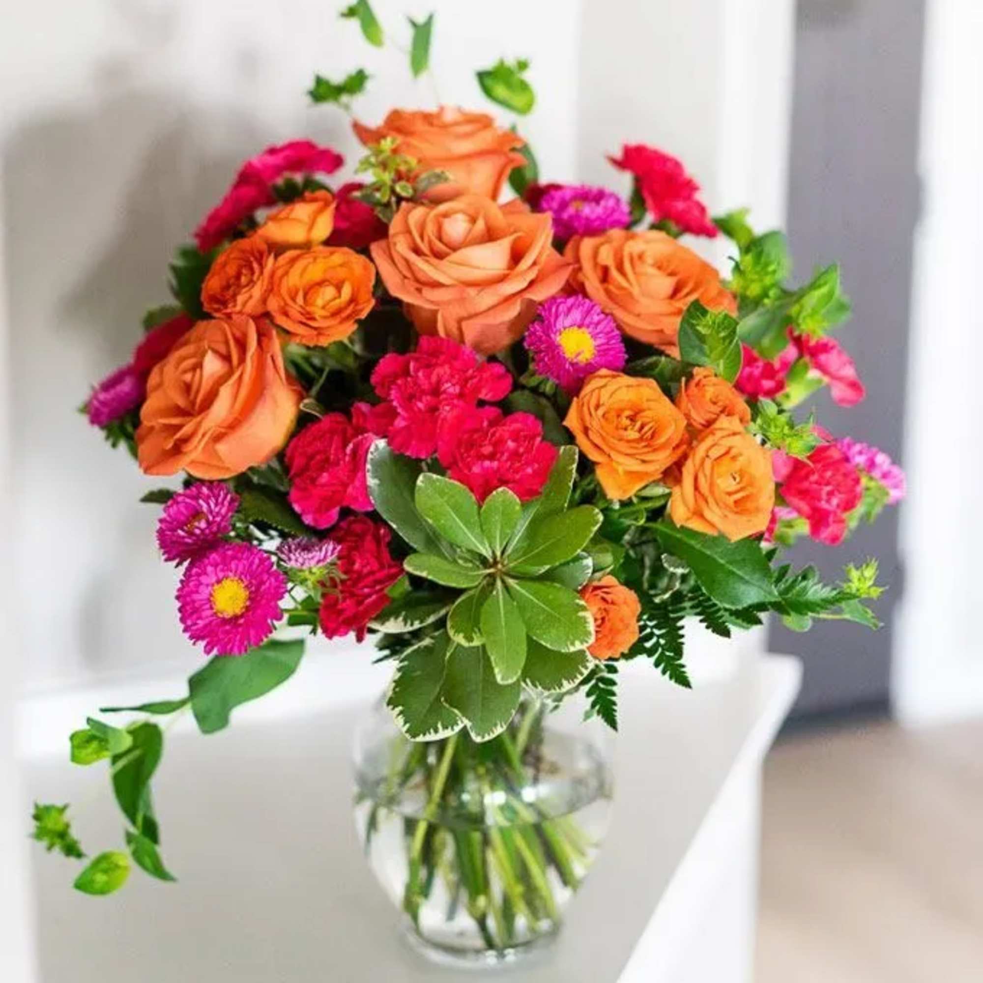 Orange roses and pink flowers arranged in a clear glass vase