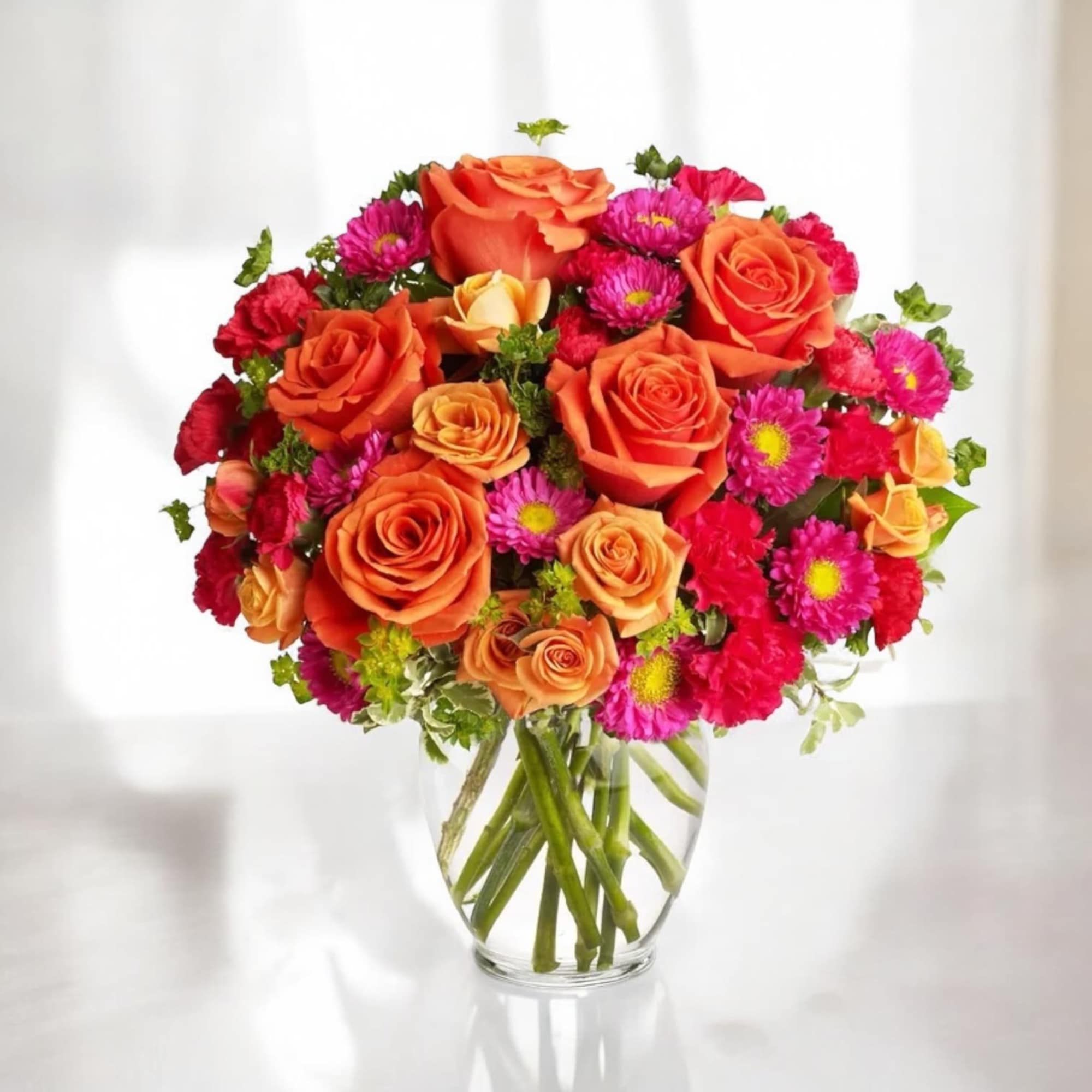 Bouquet of orange roses and pink daisies in a clear glass vase