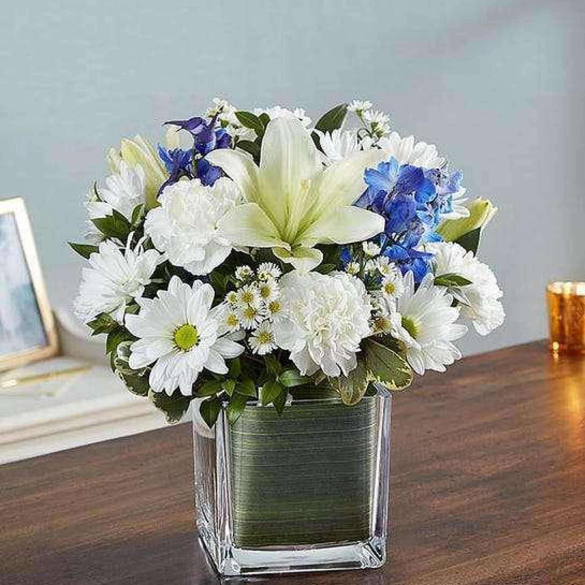 White and blue flower arrangement in a clear square vase