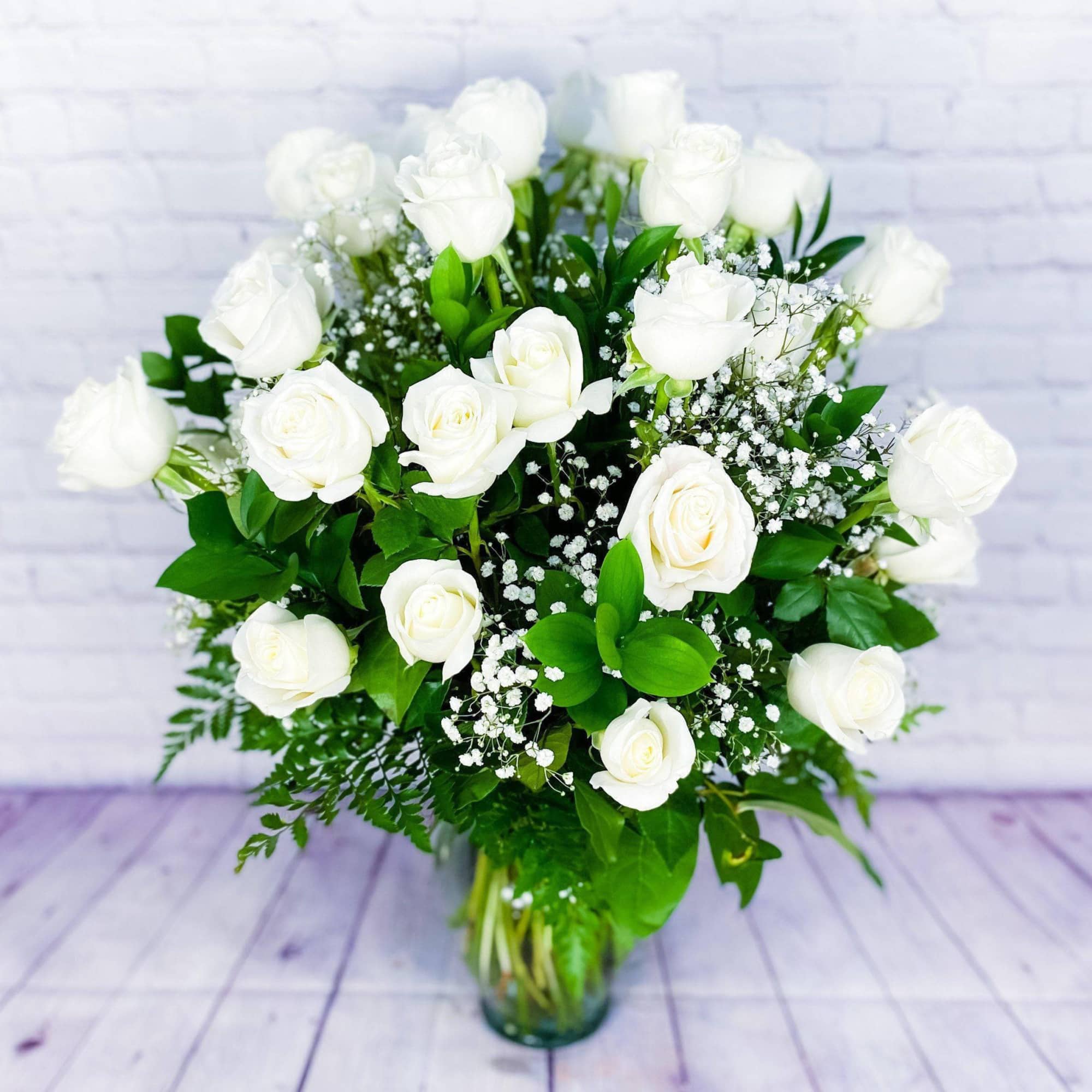 White roses arranged in a glass vase with baby's breath and greenery