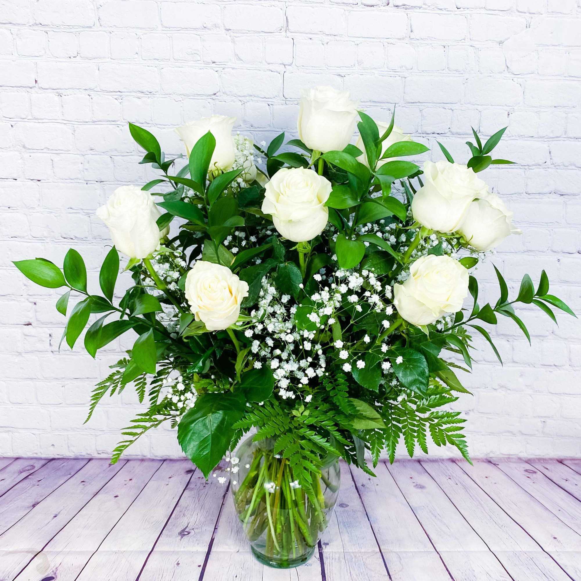 White roses in a glass vase with baby's breath and greenery