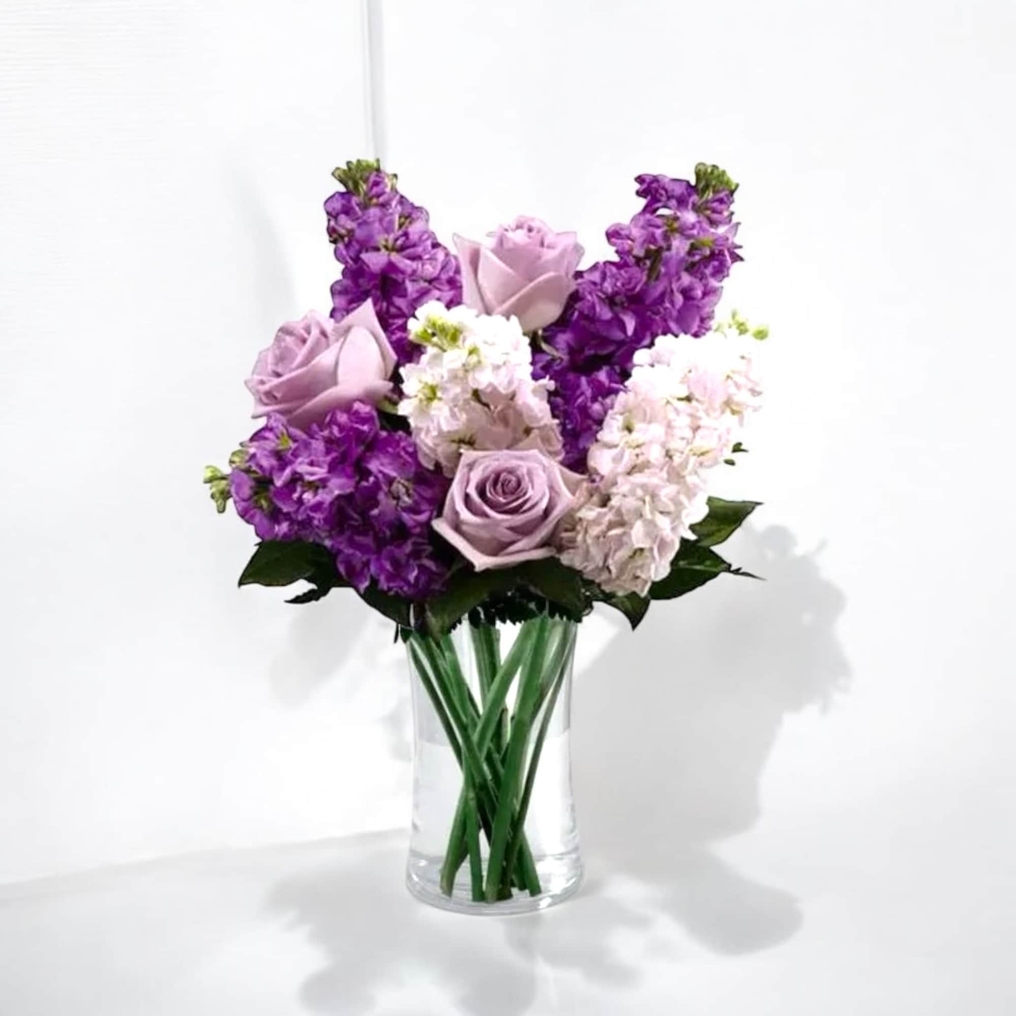 Purple and pale pink roses arranged in a clear glass vase