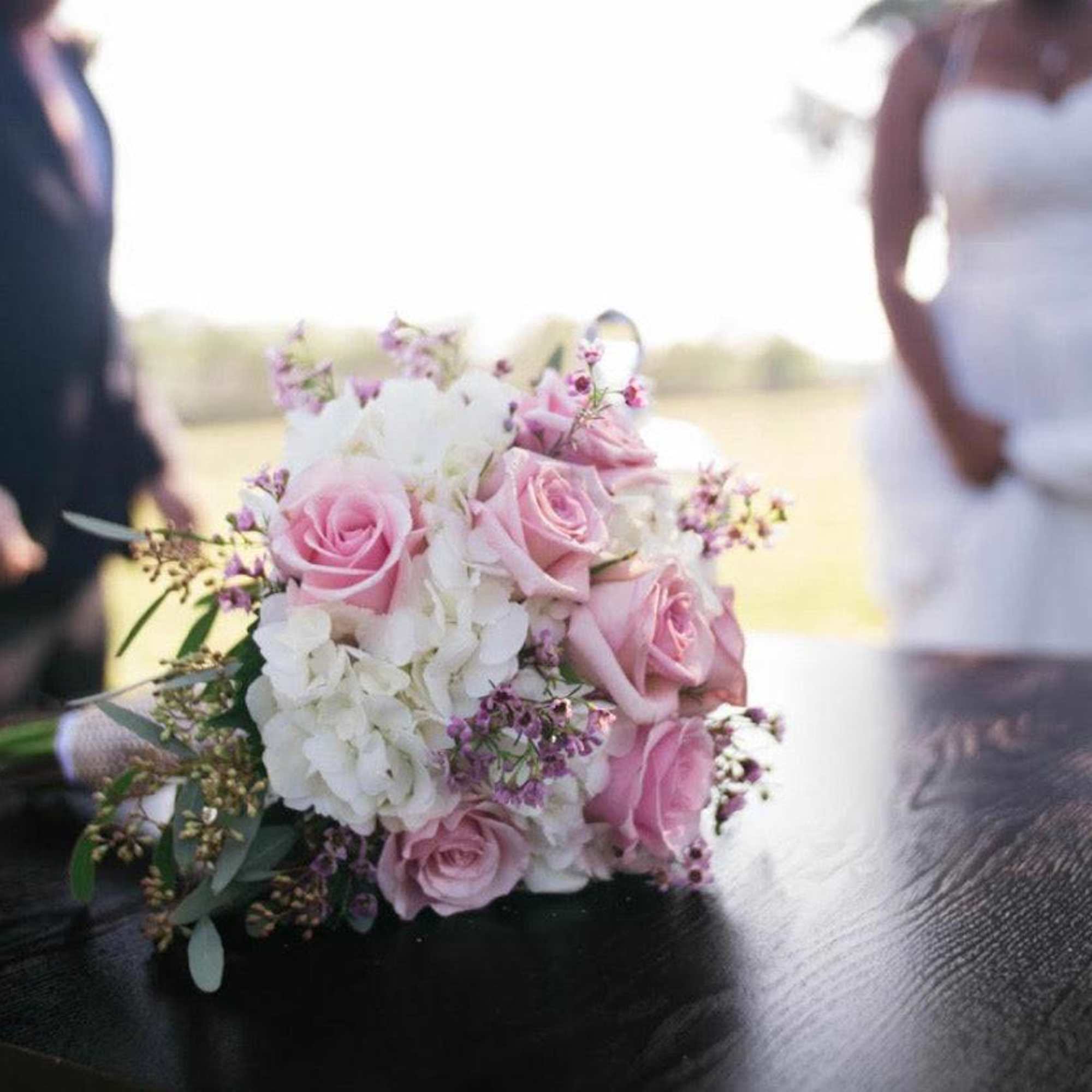 Pink and white bridal bouquet on a table with a bride and groom blurred in the background