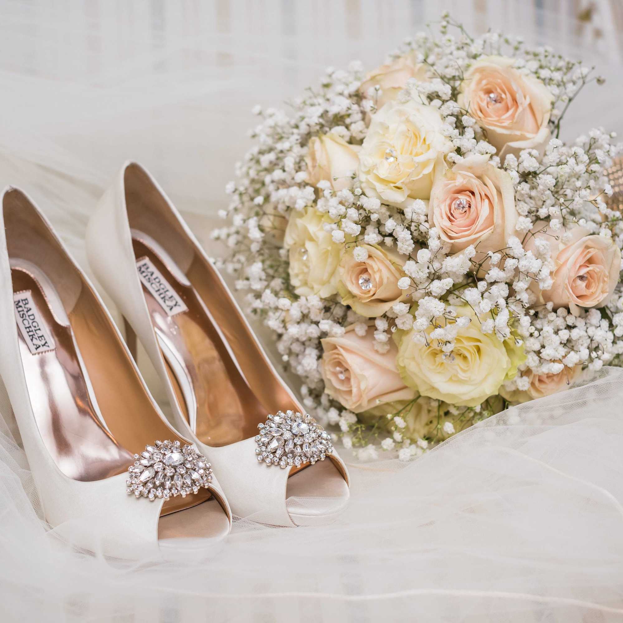 Ivory bridal heels beside a bouquet of pale roses and baby's breath