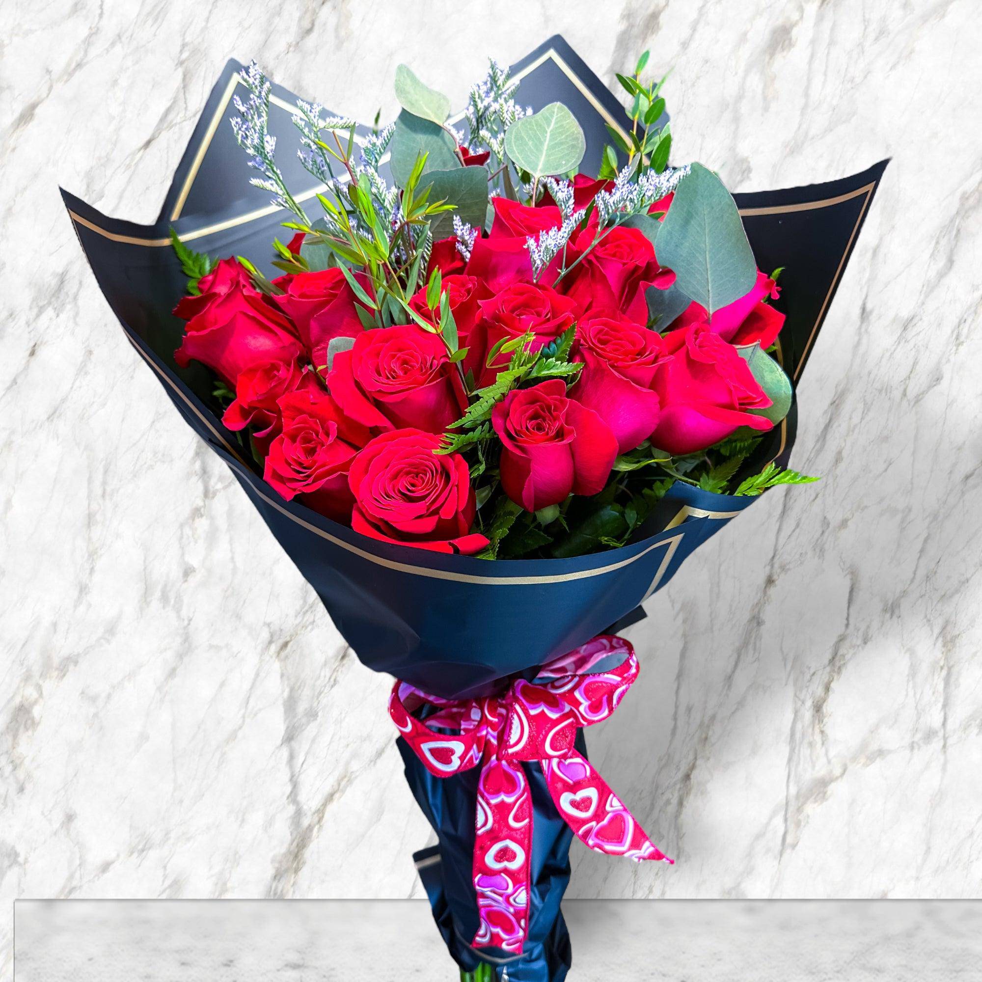 Bouquet of red roses wrapped in dark paper with a pink heart ribbon