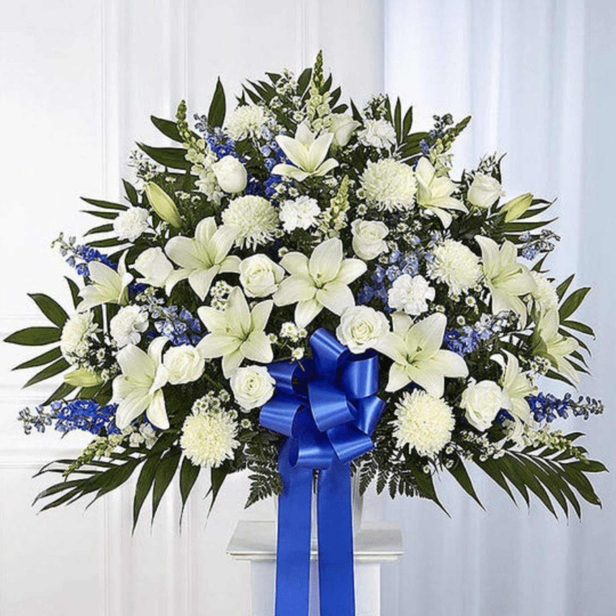 White floral standing spray with blue ribbon on a pedestal