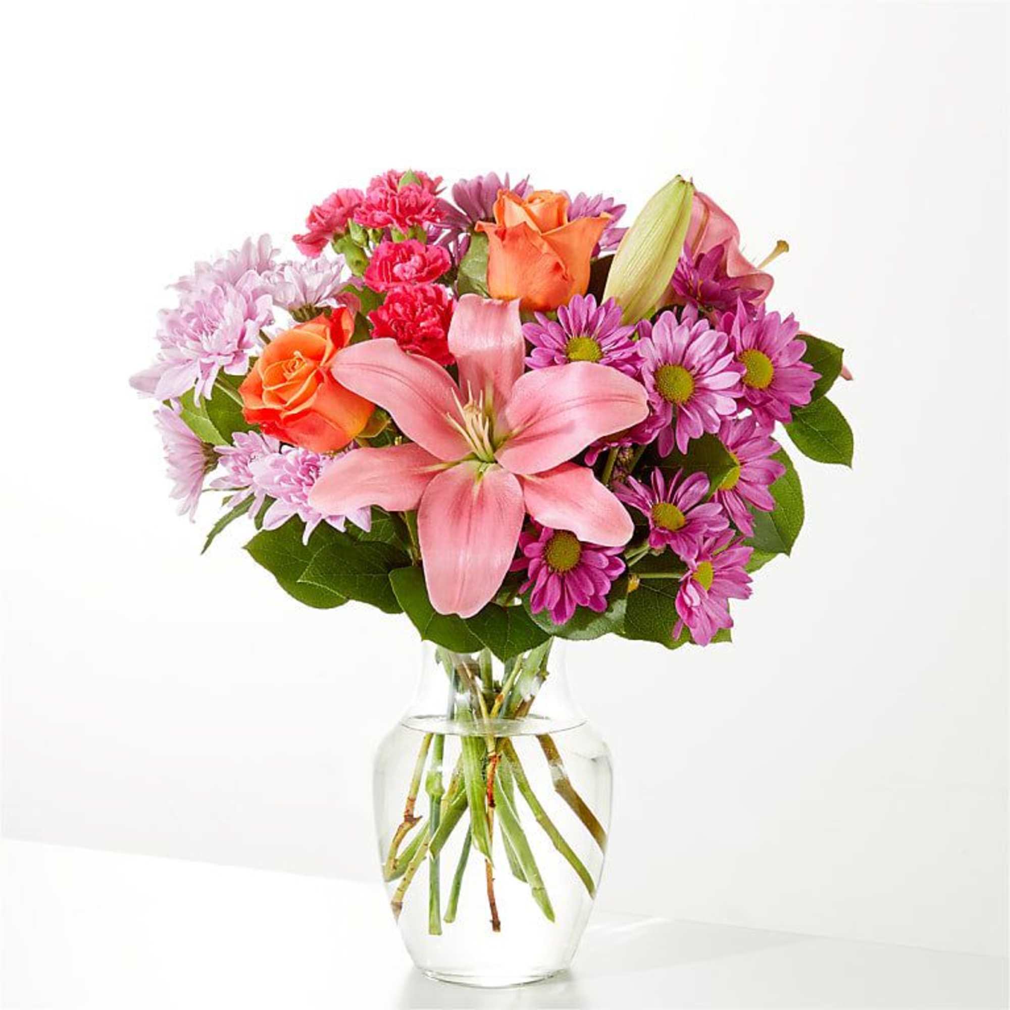 Pink lilies and mixed pink-orange flowers in a clear glass vase