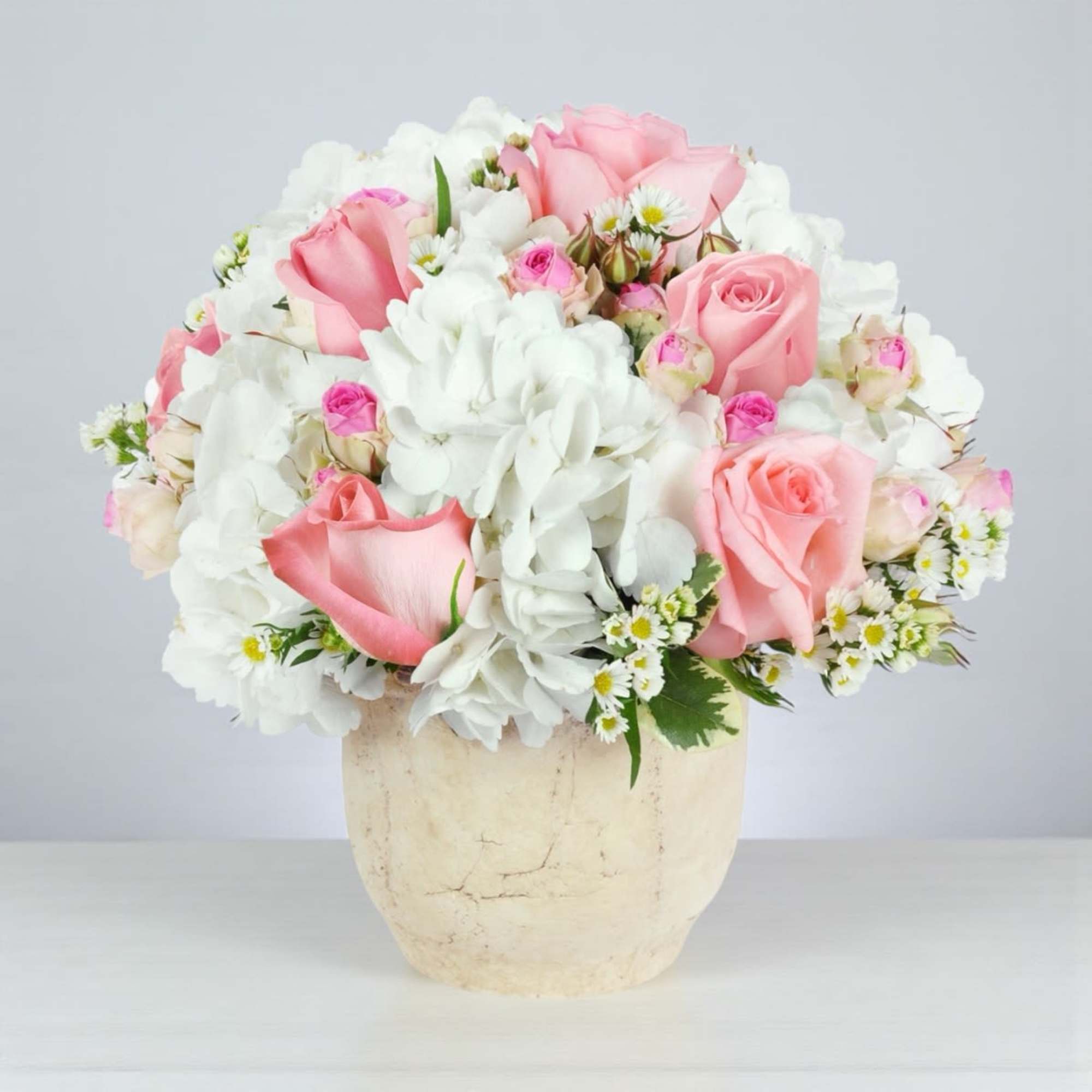 Pink roses and white flowers arranged in a cream vase