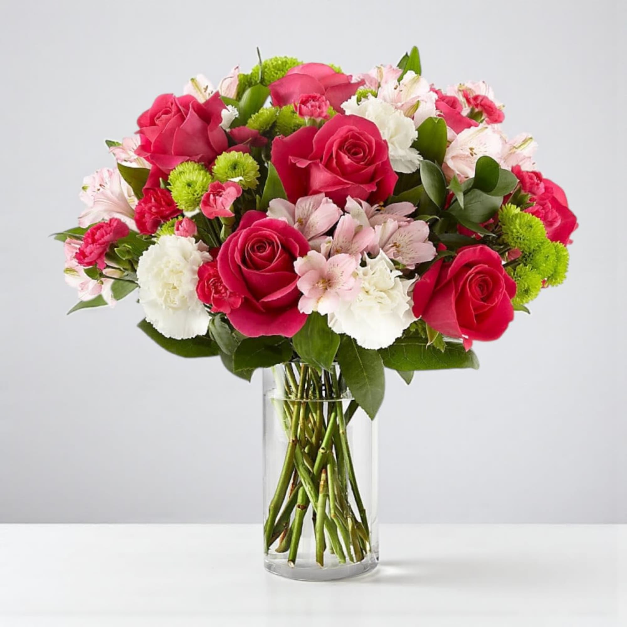 Bouquet of pink roses, white carnations, and green pompons in a clear glass vase