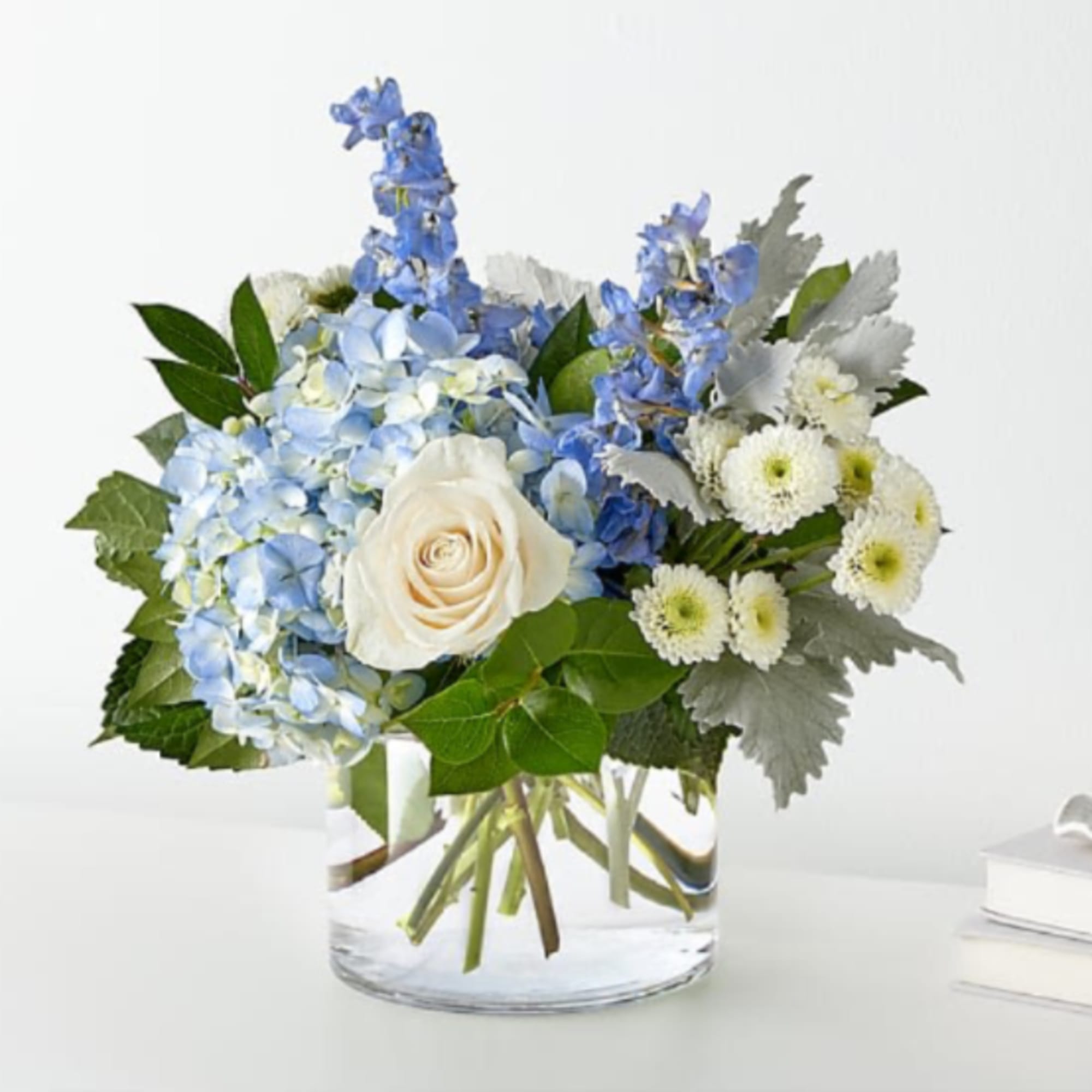 Blue hydrangeas, white rose, and white daisies in a clear glass vase