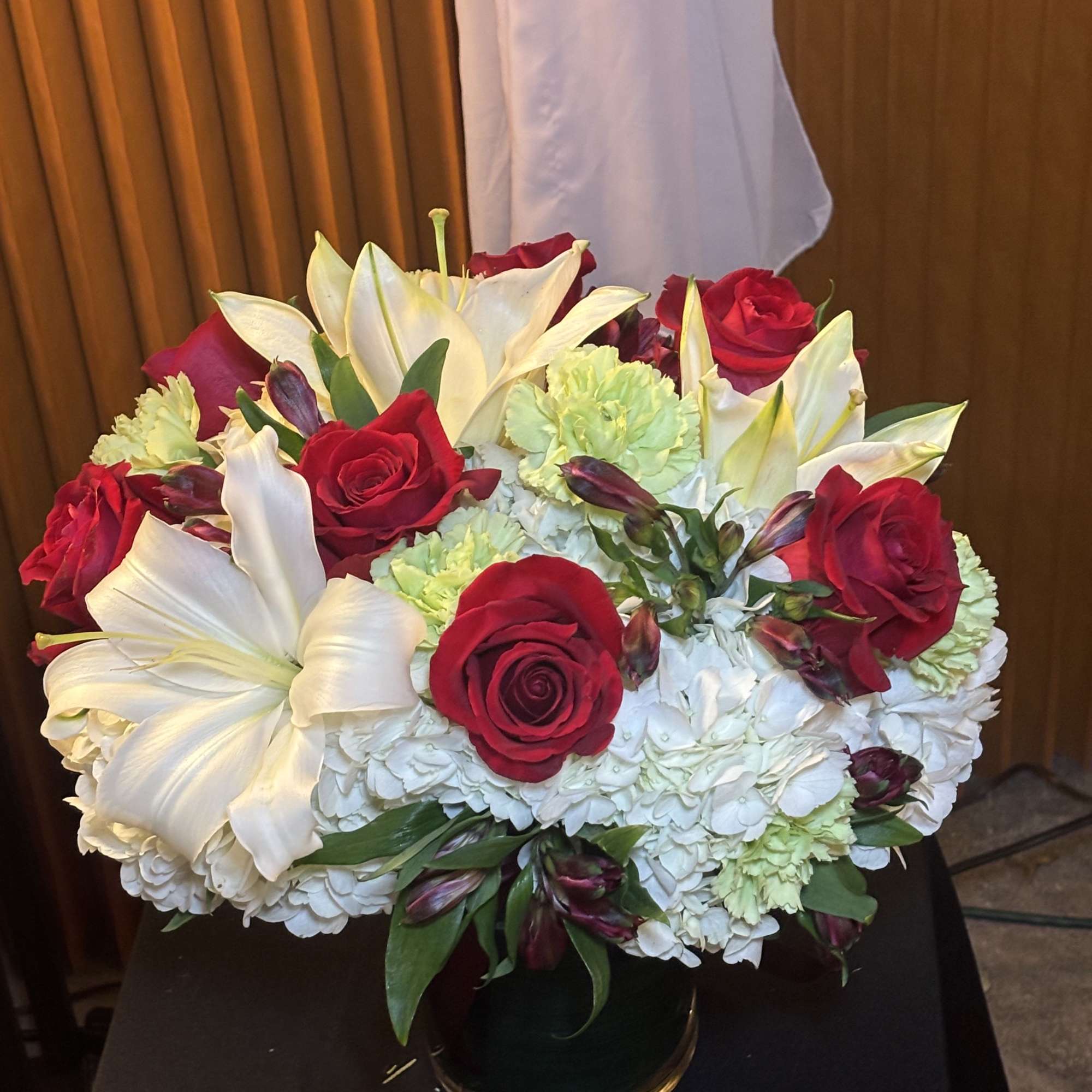 Red roses and white lilies arranged in a low vase with white hydrangeas