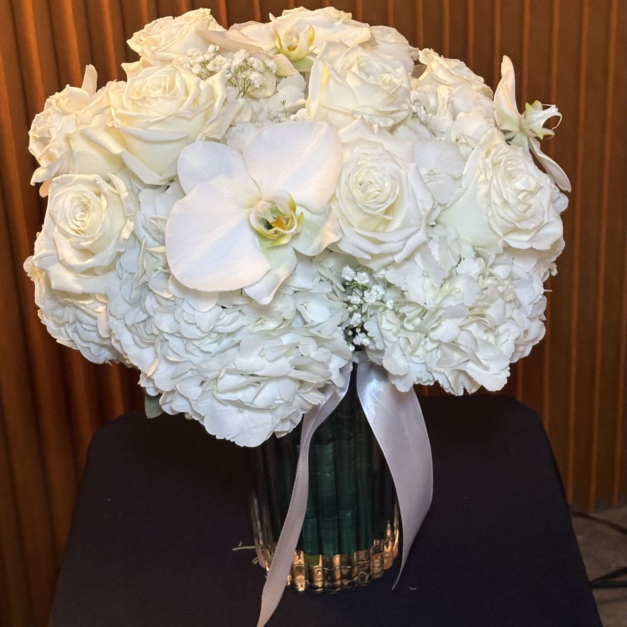 White roses and orchids arranged in a glass vase with a ribbon
