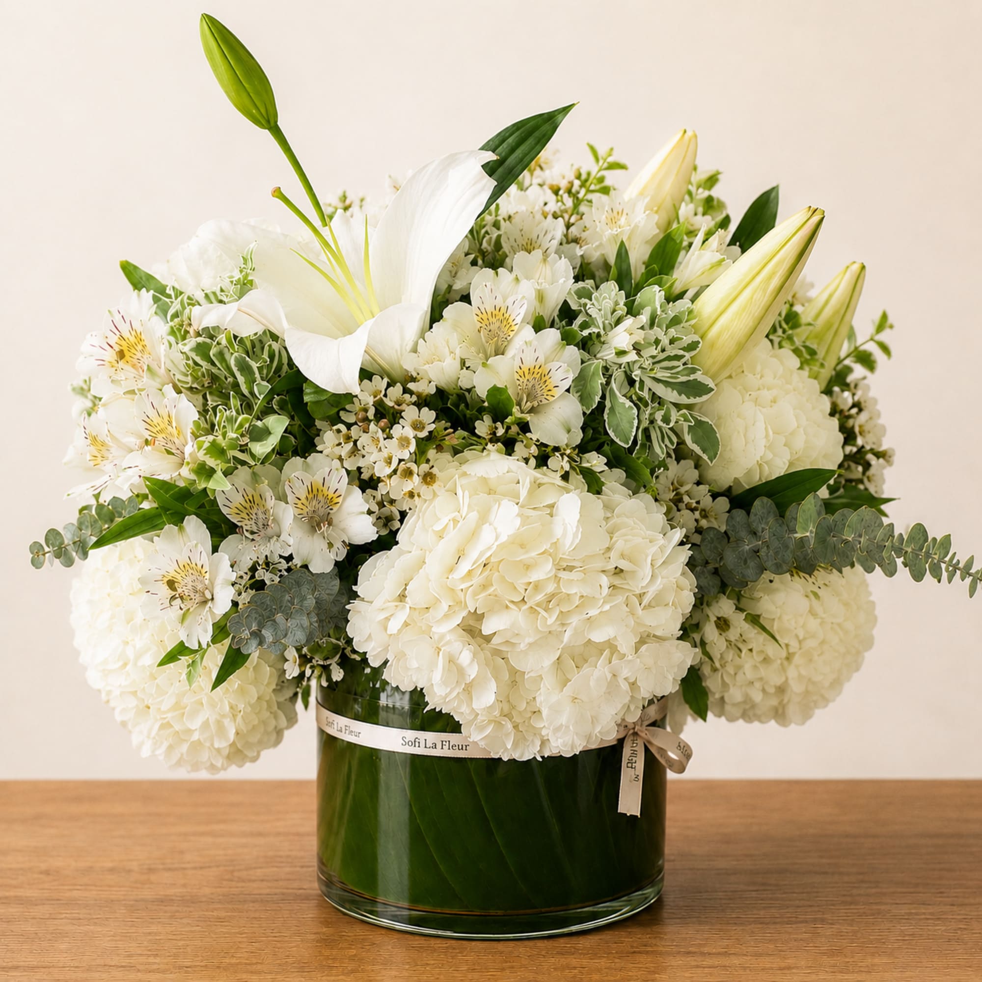 White floral arrangement in a glass vase with lilies and hydrangeas